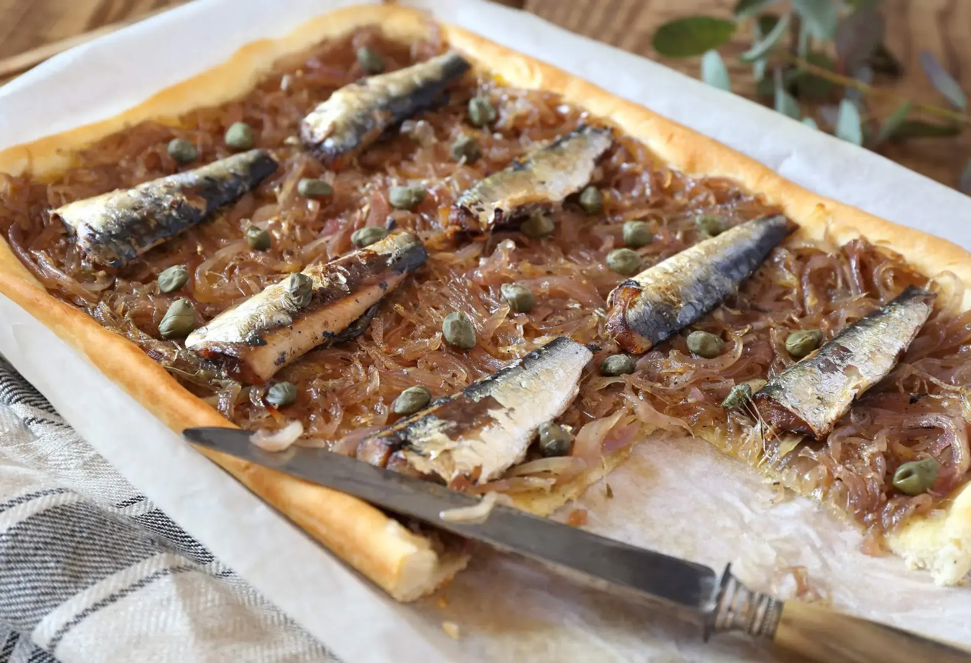 Pissaladière with sardines on a white paper with a knife