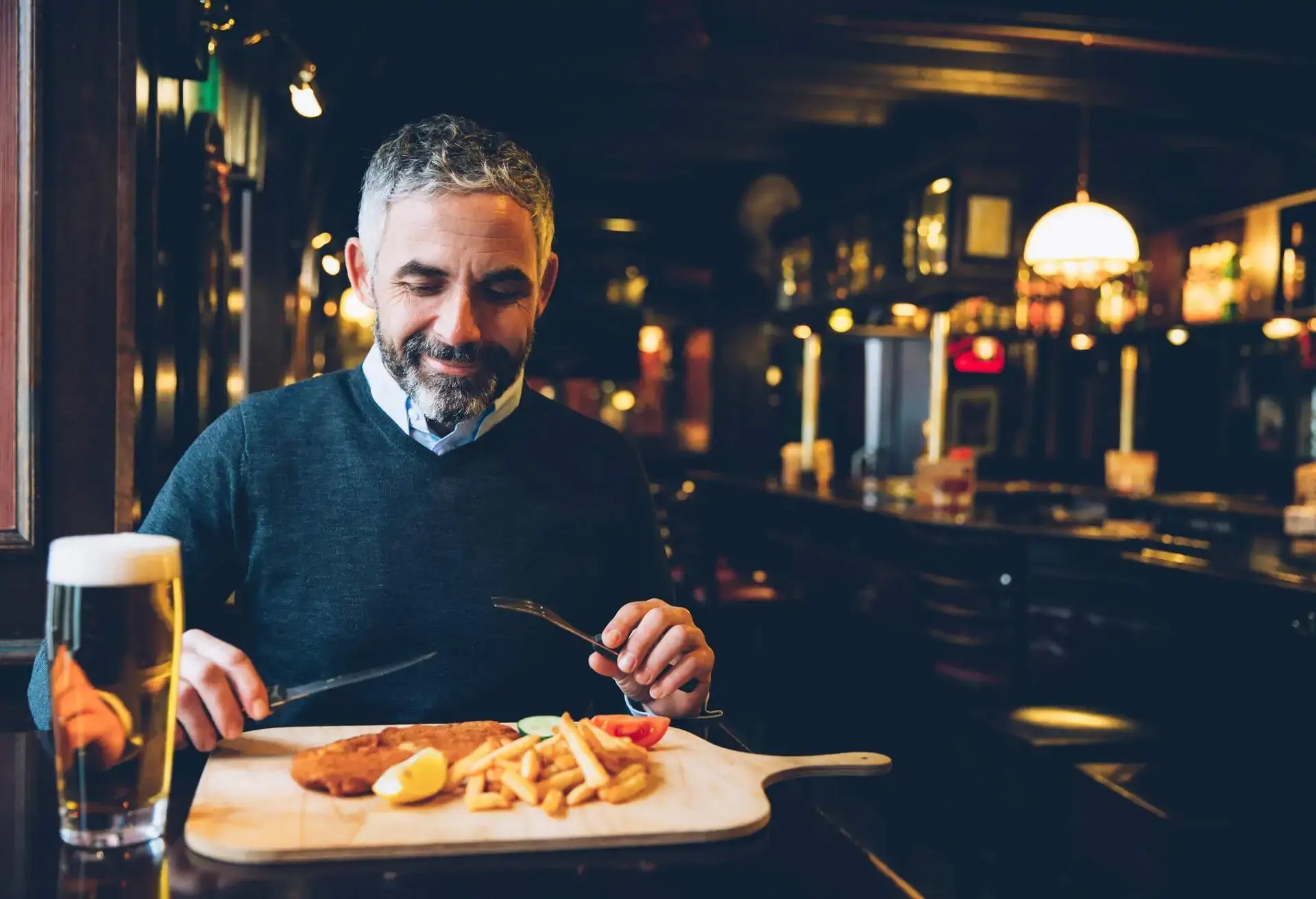 Man sitting in a restaurant at a table with a wooden board with Schnitzel, french fries and a beer in front of him