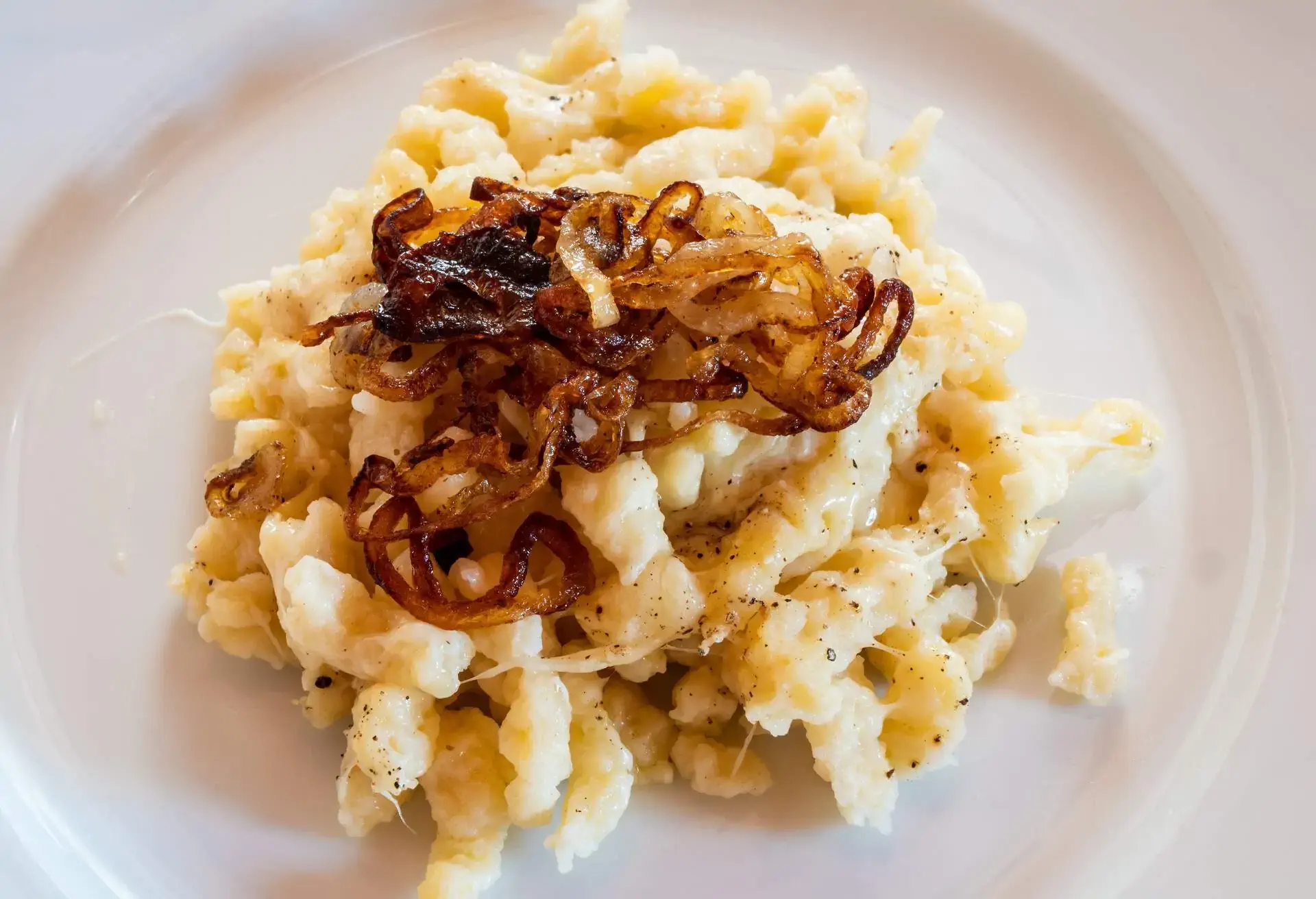 White plate with Käsespätzle and fried brown onions on top