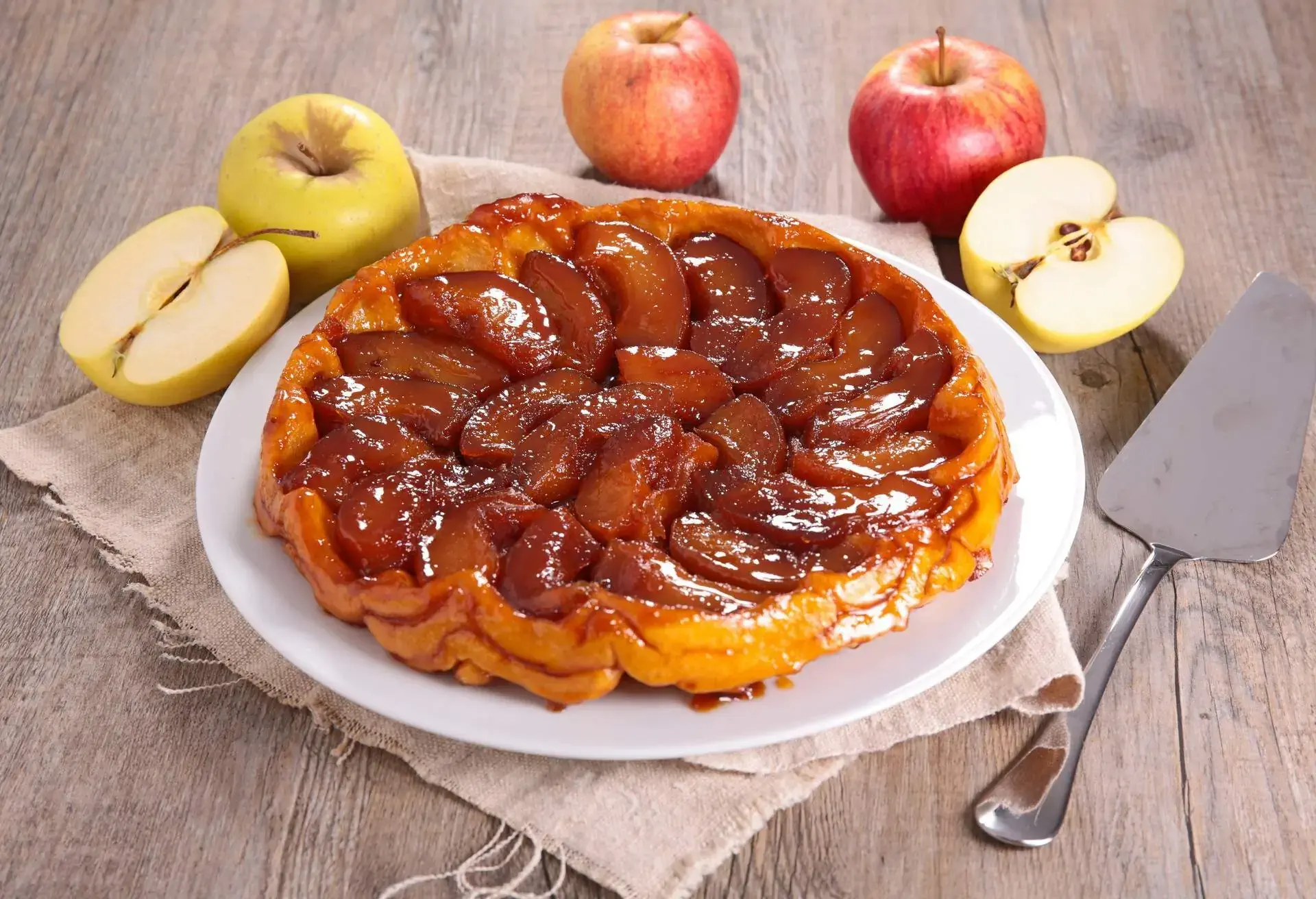 Tarte Tatin on a white plate on a wooden table surrounded by apples