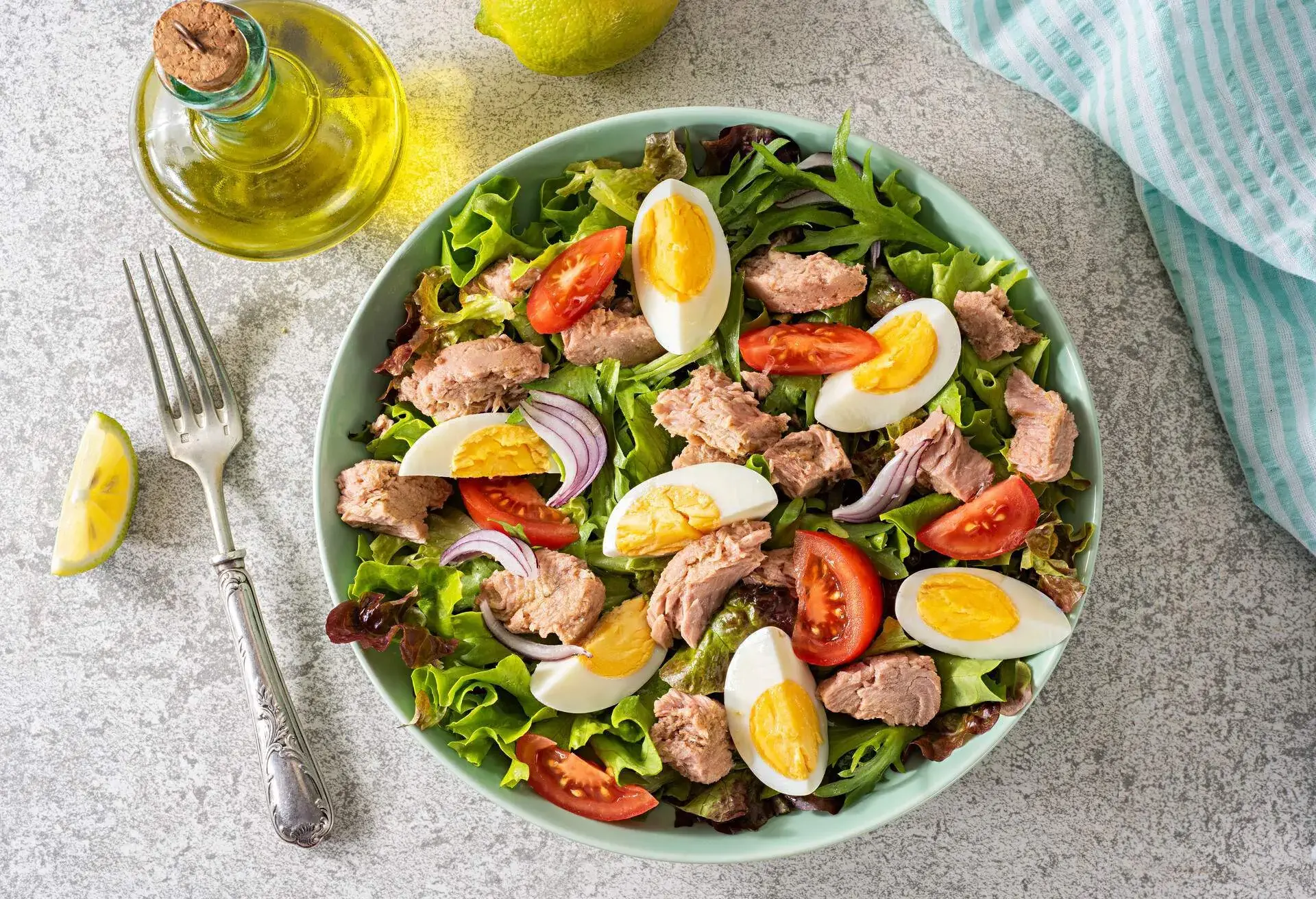 Bowl of Salade Niçoise with fork and bottle of oil next to it