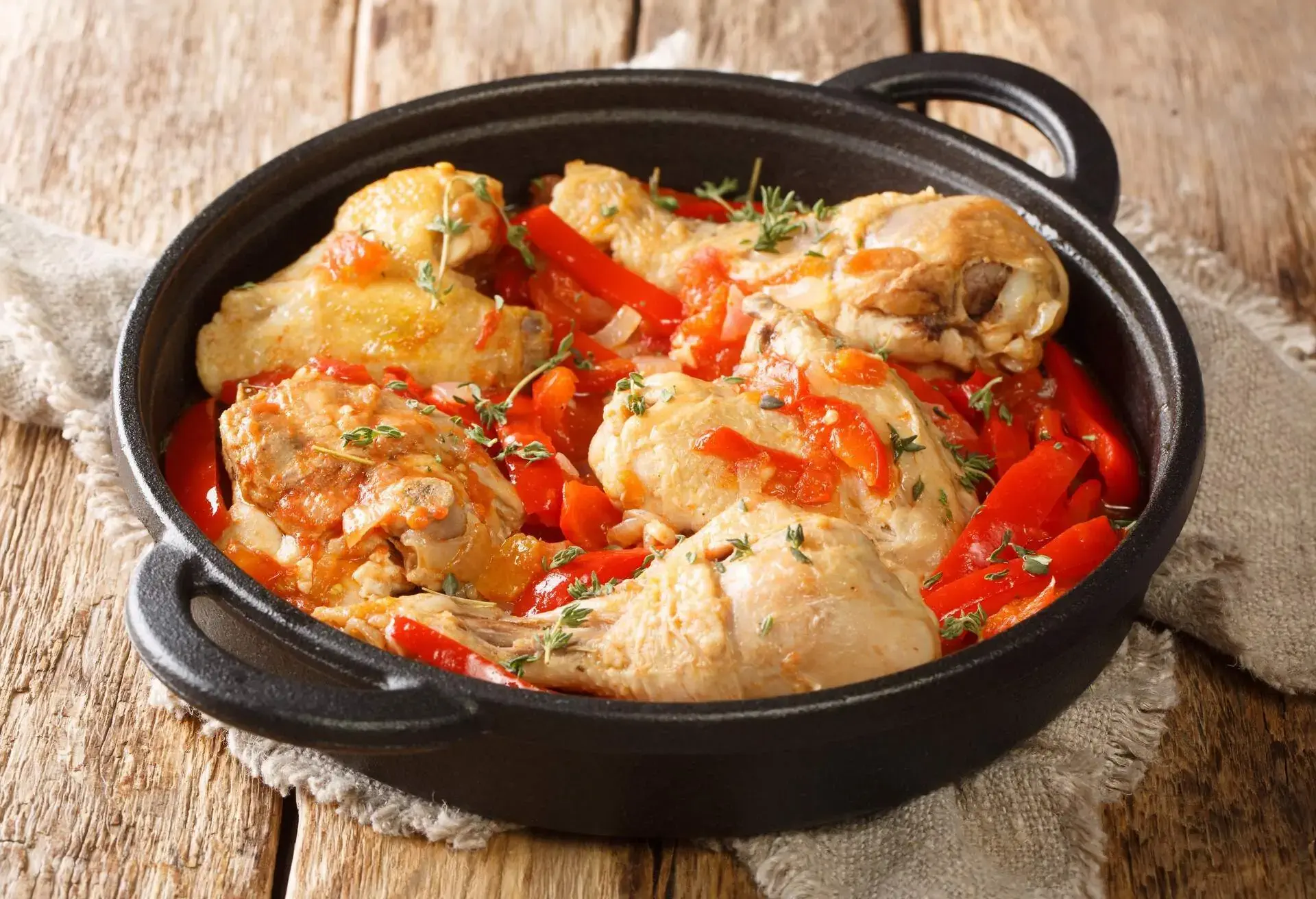Black pot with Poulet Basquaise on a rough napkin on a wooden table