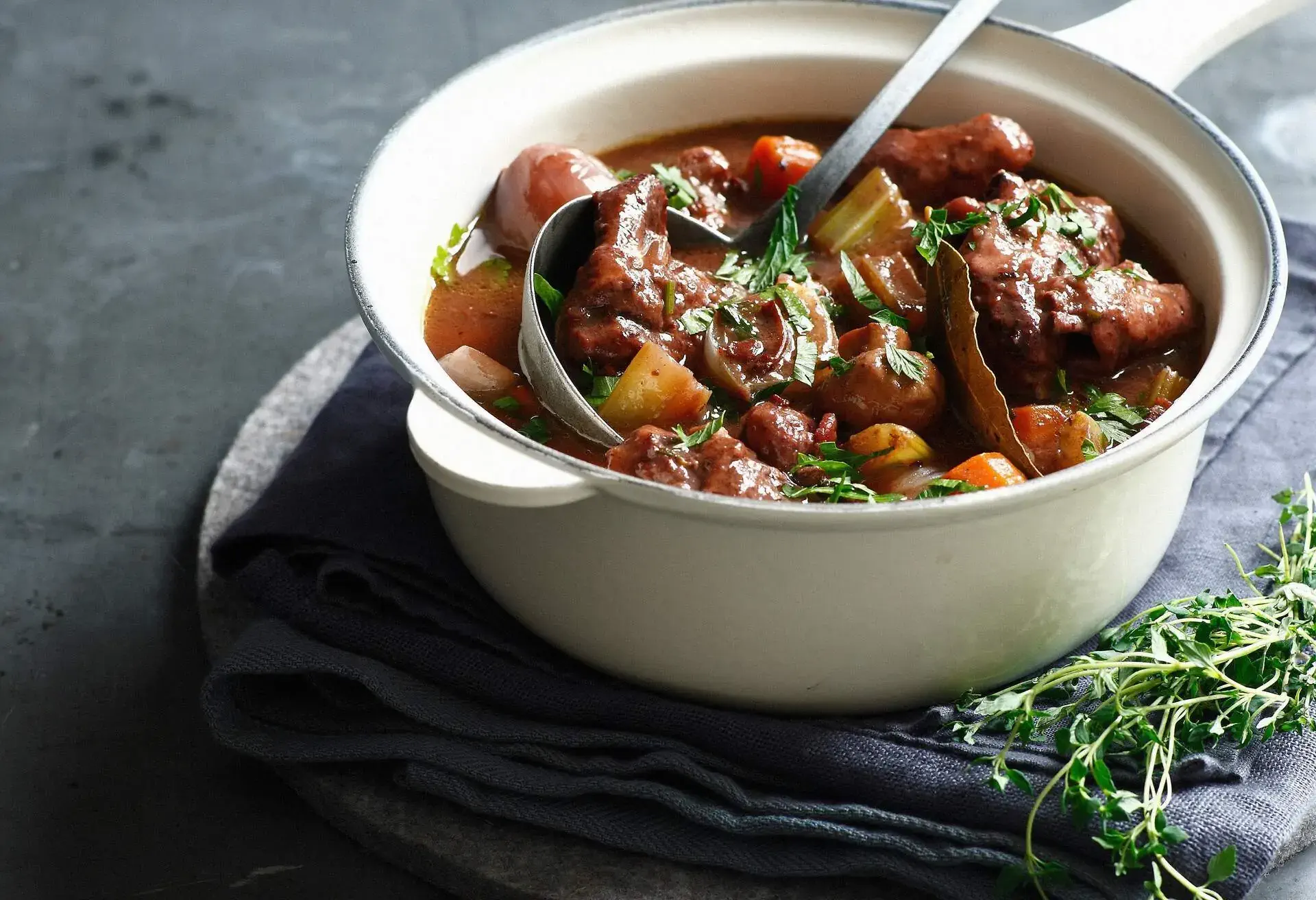 White pot with Boeuf Bourguignon and ladle with herbs on the side