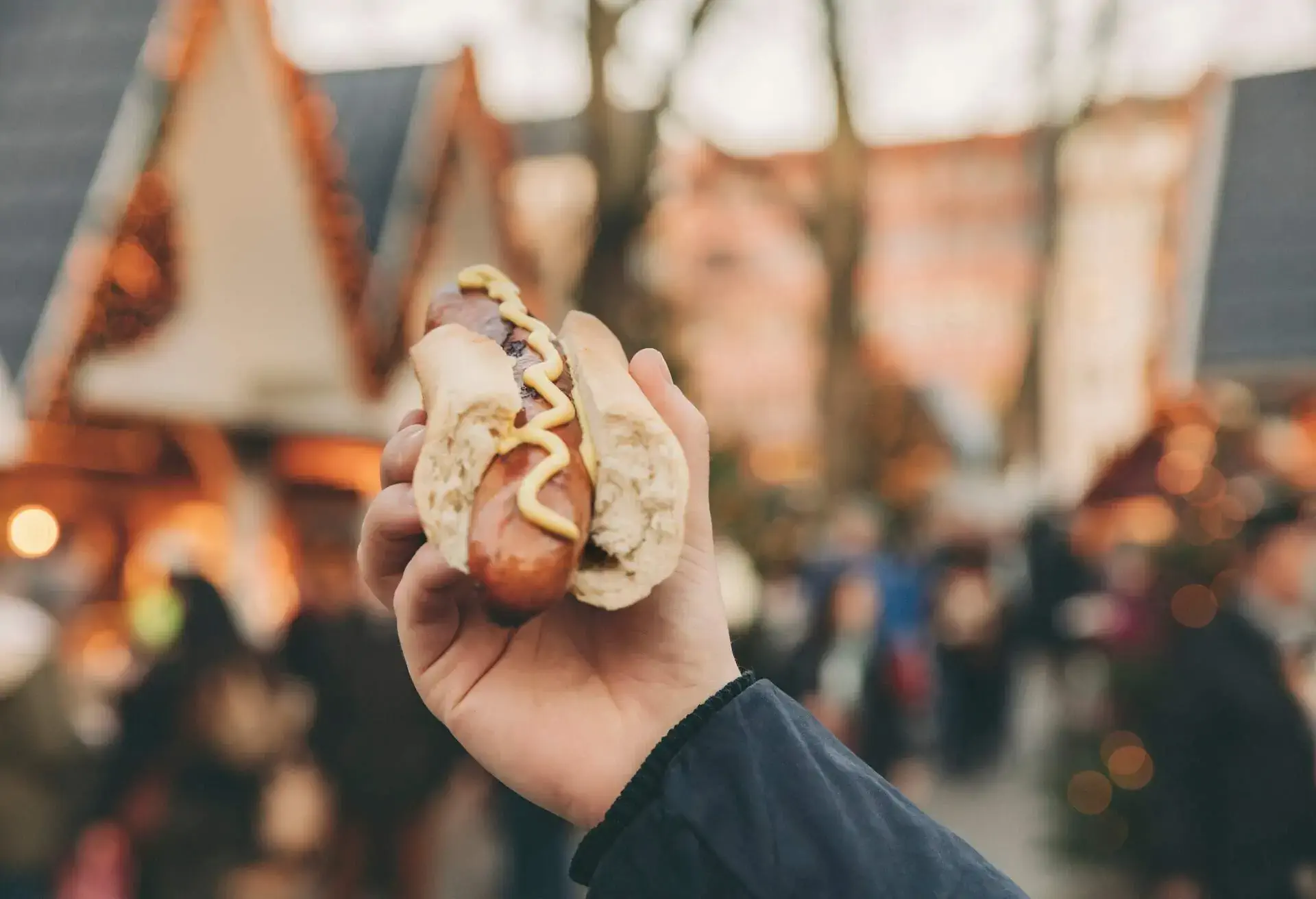 Hand holding Bratwurst in a roll with mustard