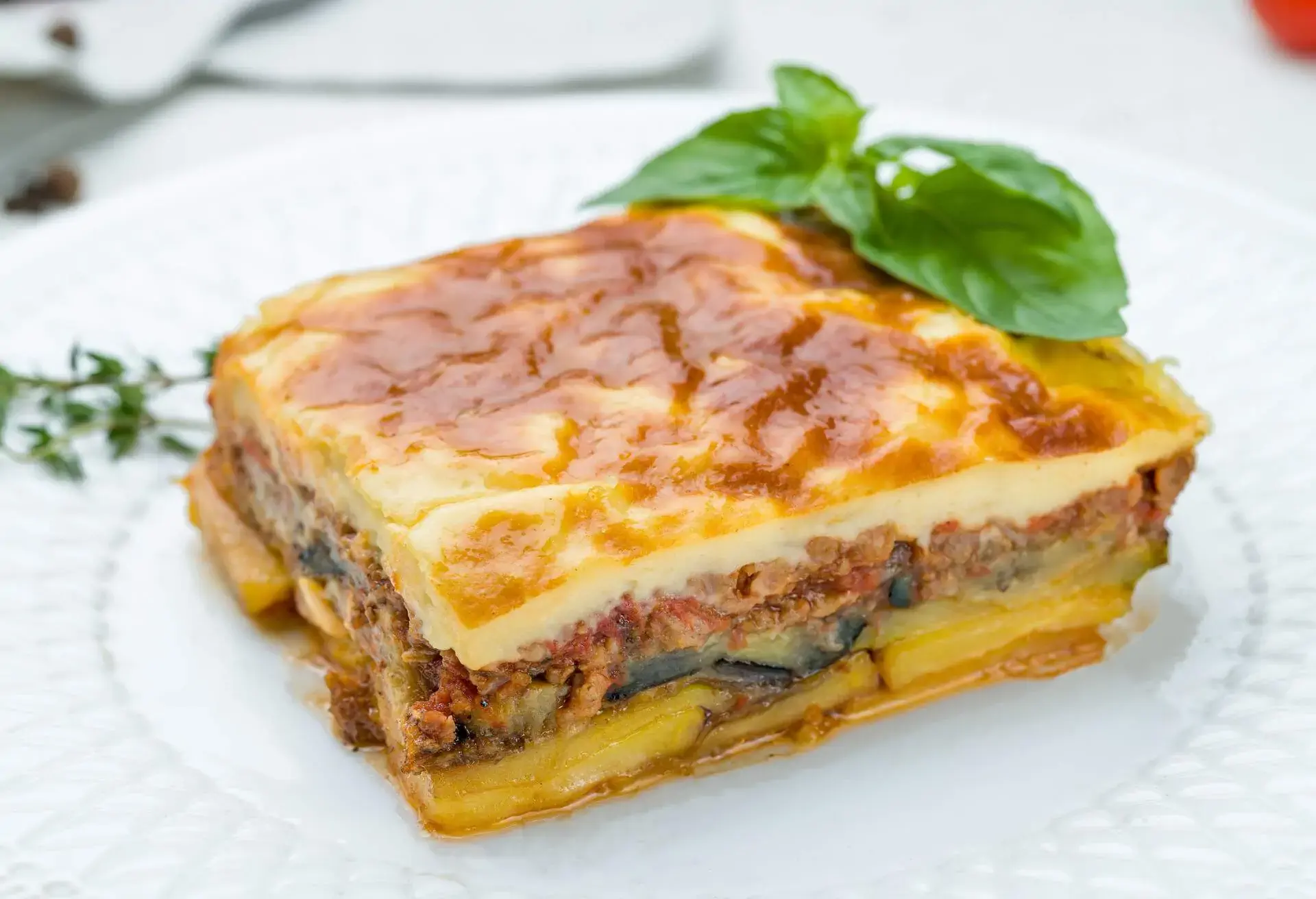 Moussaka on a white plate decorated with basil leaf