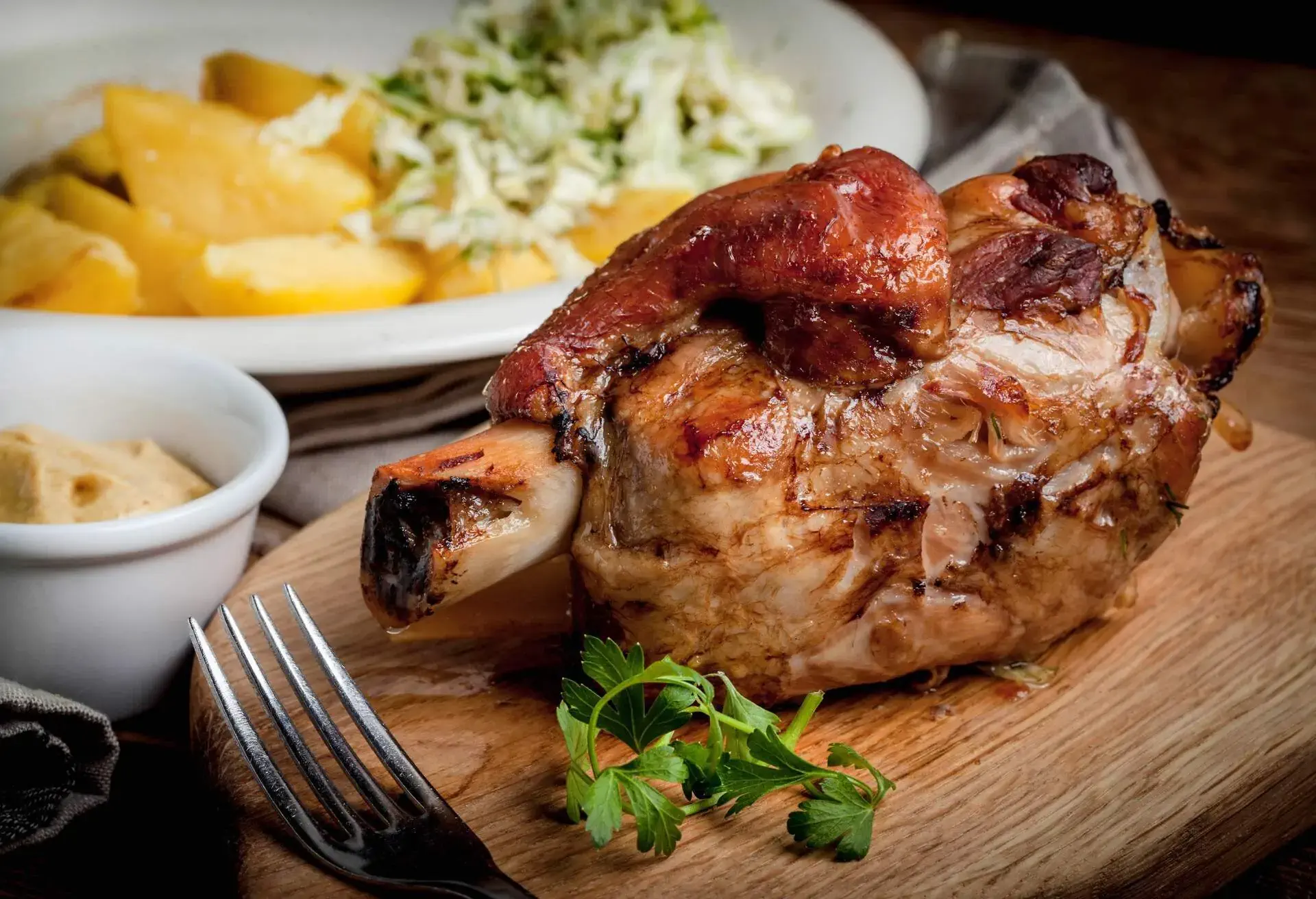 Schweinshaxe on a wooden board with a white bowl and potatos