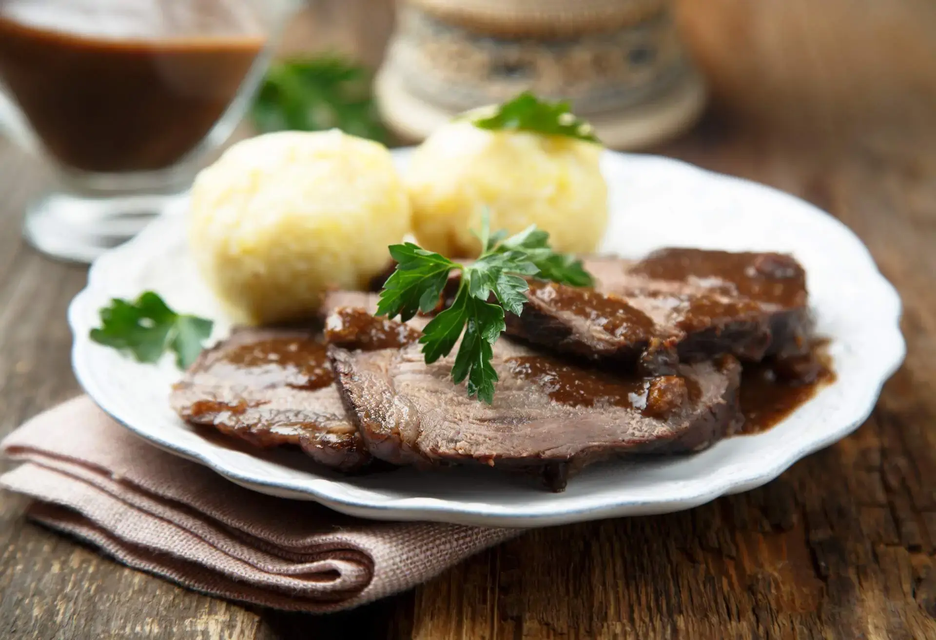 White plate with slices of Sauerbraten and potato dumplings