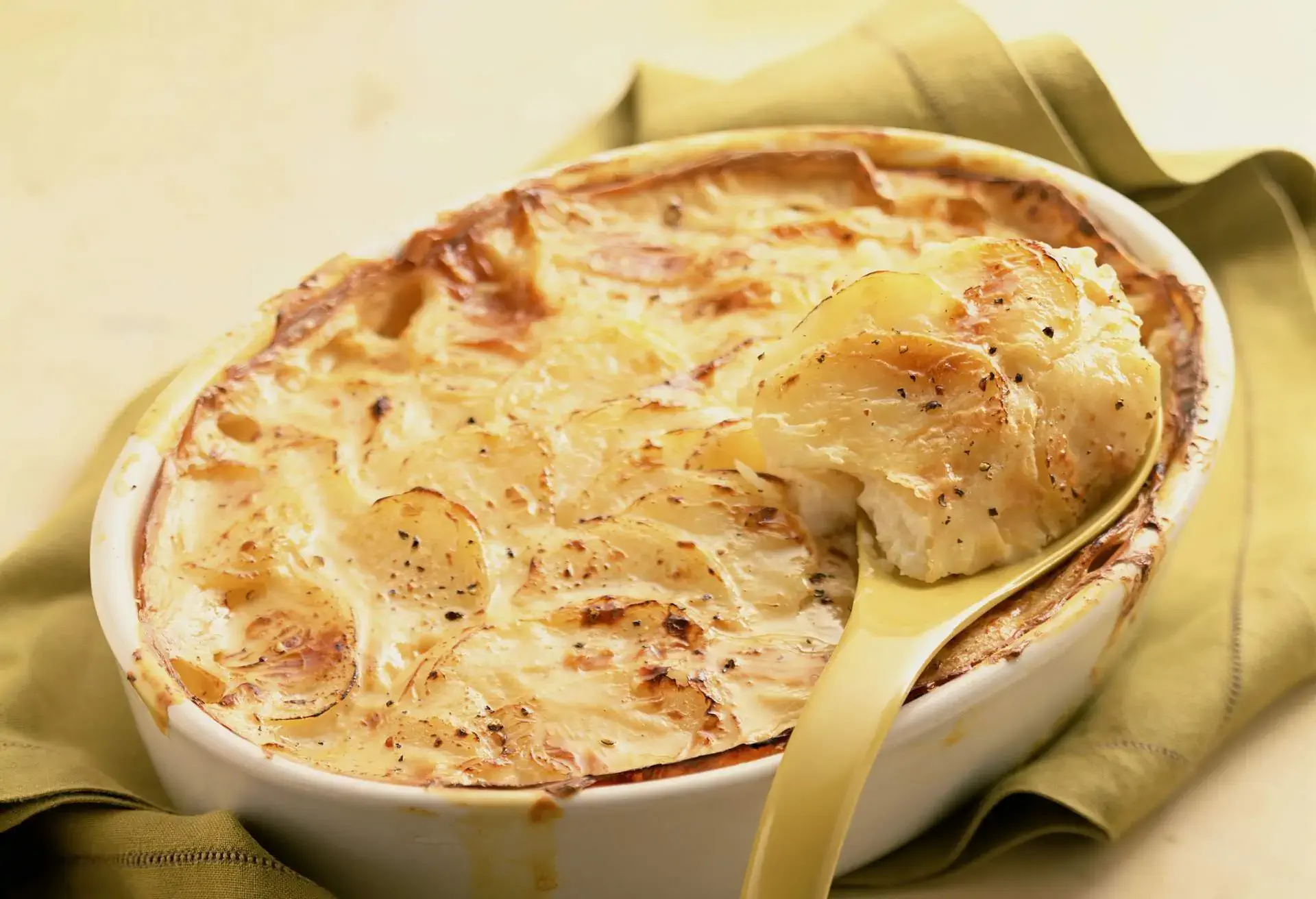 Dauphinoise Potatoes in a white dish with a ladle
