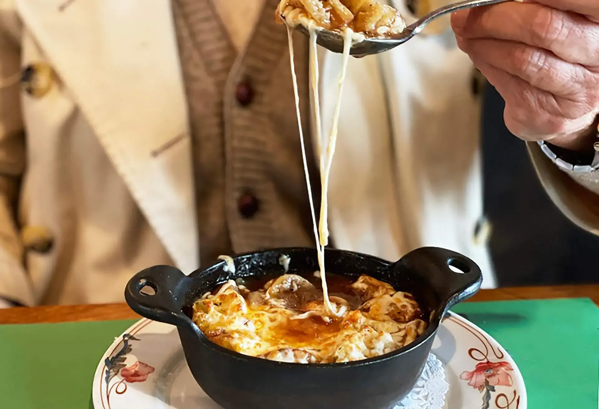 Hand scouping up French onion soup with cheese strings from a black bowl