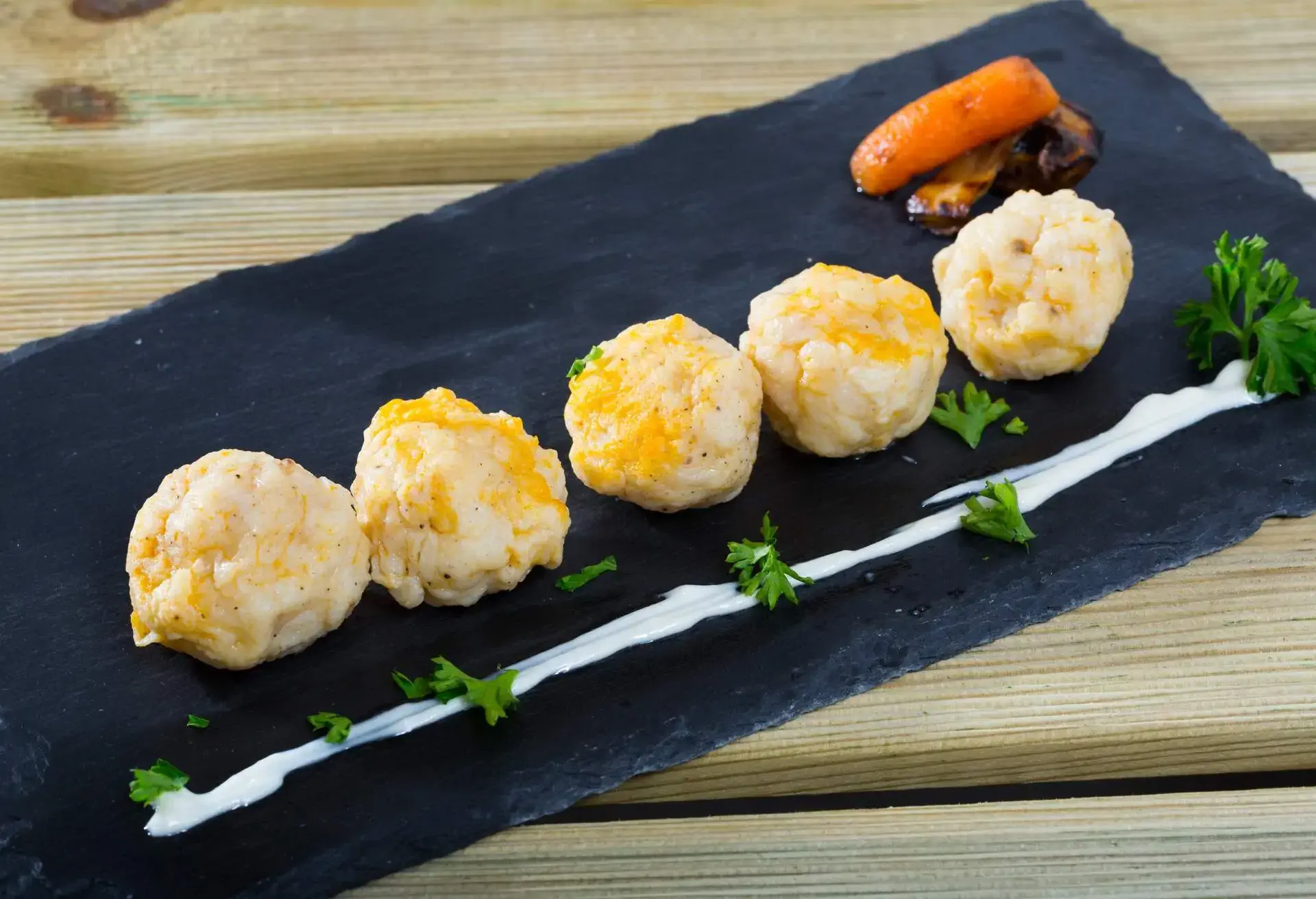 Traditional Norwegian Fiskeboller served with white sauce, parsley, carrot and mushroom on black serving board 