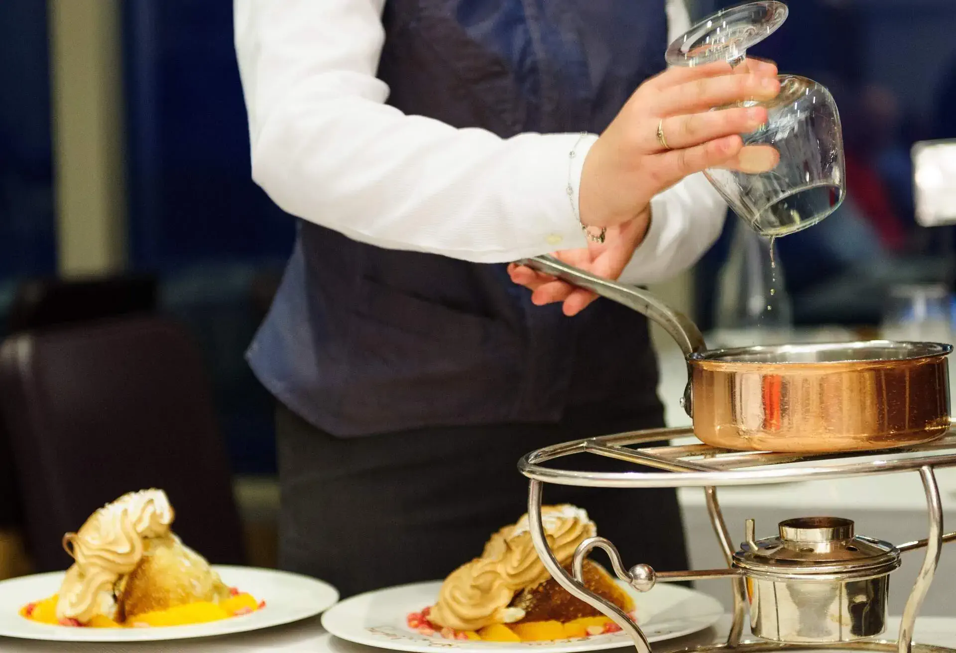 Waiter pouring a glass of alcohol over a pot with Crêpe Suzette tableside