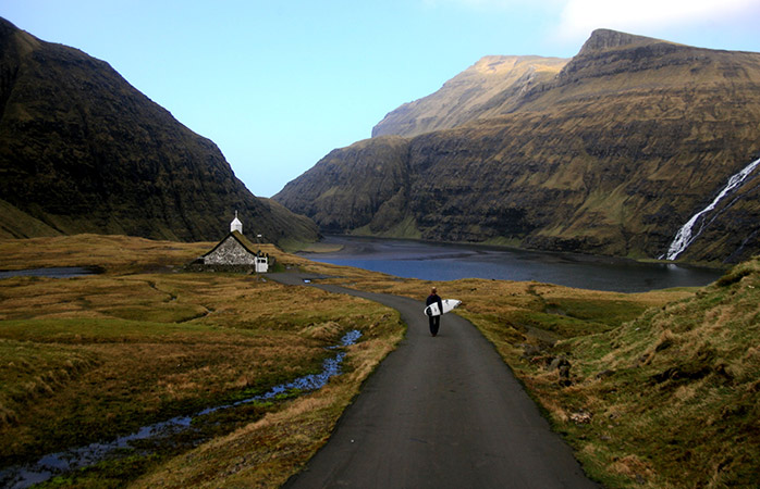 En mand med sit surfbræt i landsbyen Saksun © Sergio Villalba & Visit Faroe Islands