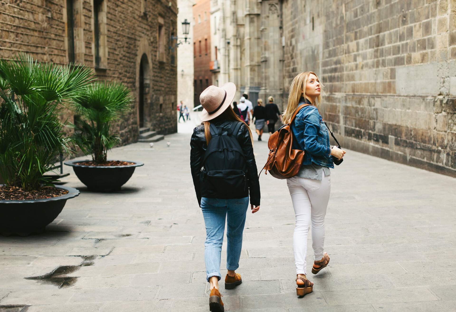 Two women in casual clothes walk while gazing up at the high walls of the street.