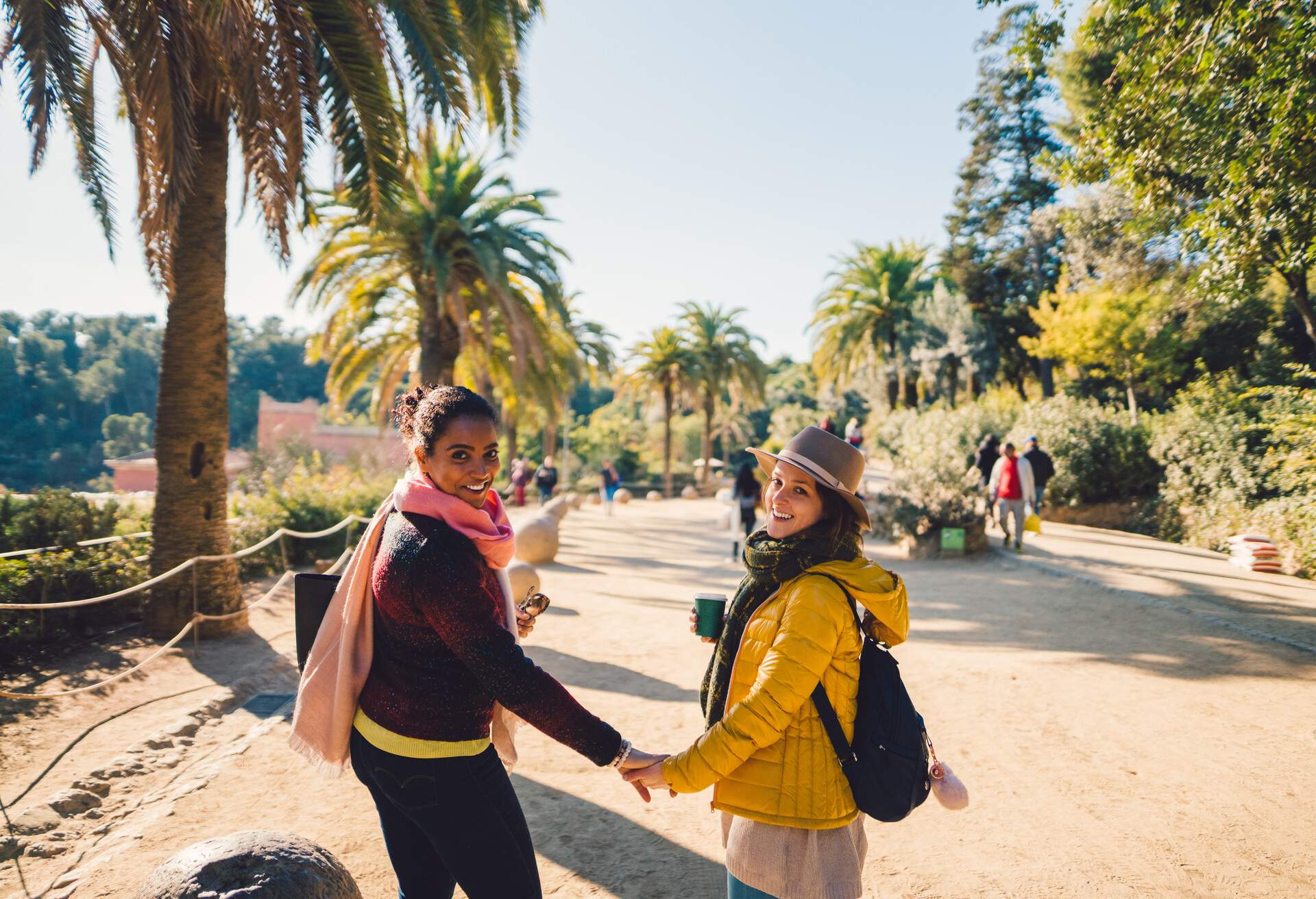 Two women wearing warm clothing holding hands as they stand in a park.