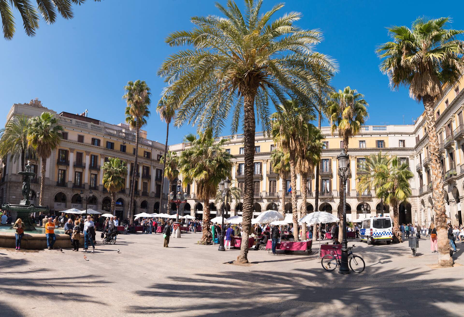 A public square with people enclosed by an arcade and dotted with trees.