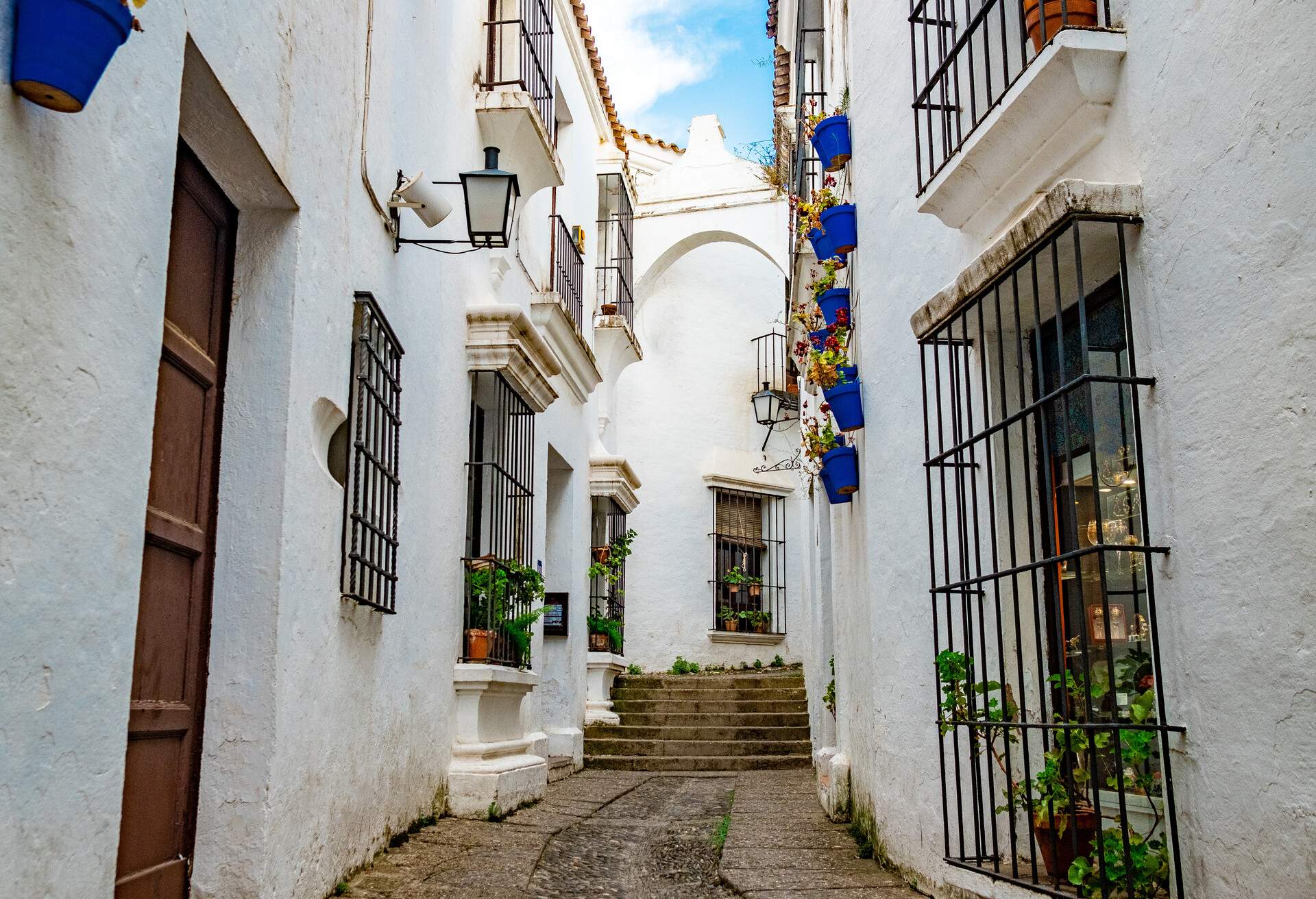 White stucco buildings with ironworks over the windows surrounding a narrow alley.