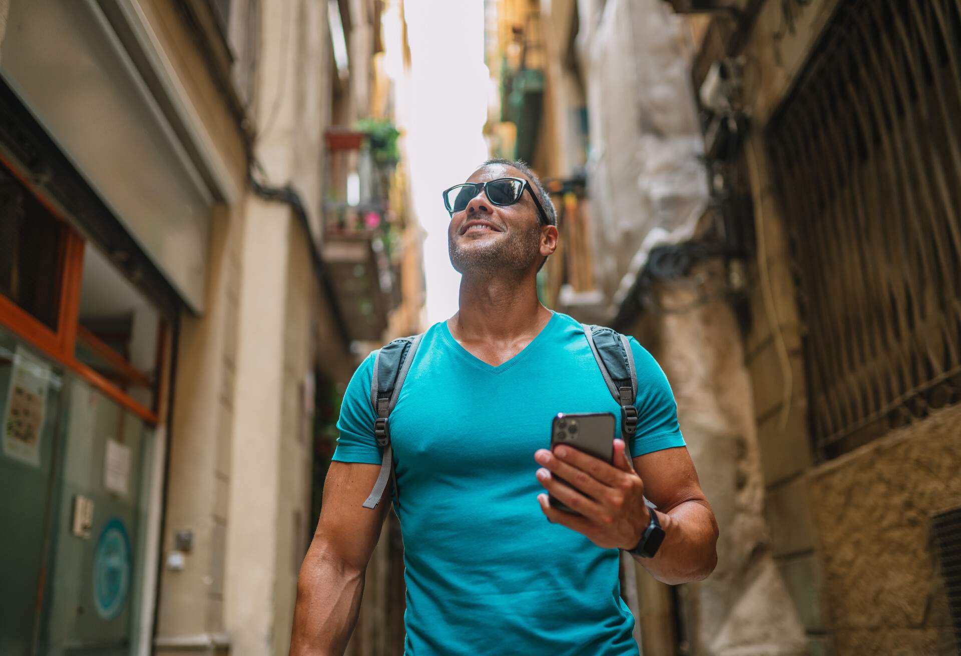 Smiling man holding his smartphone while roaming an old town street.