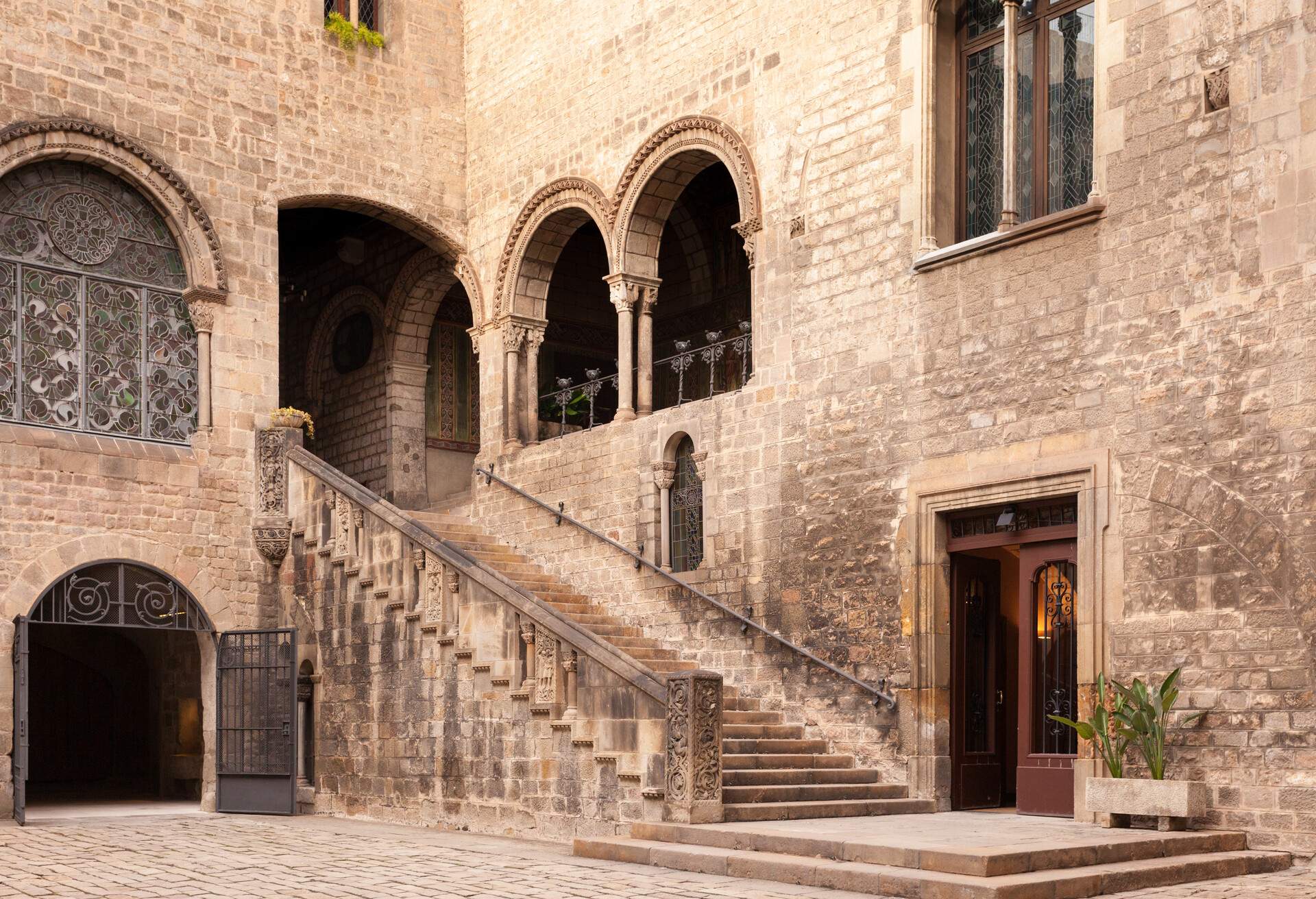 A central patio with an exterior stairway of a stone structure with arched windows.