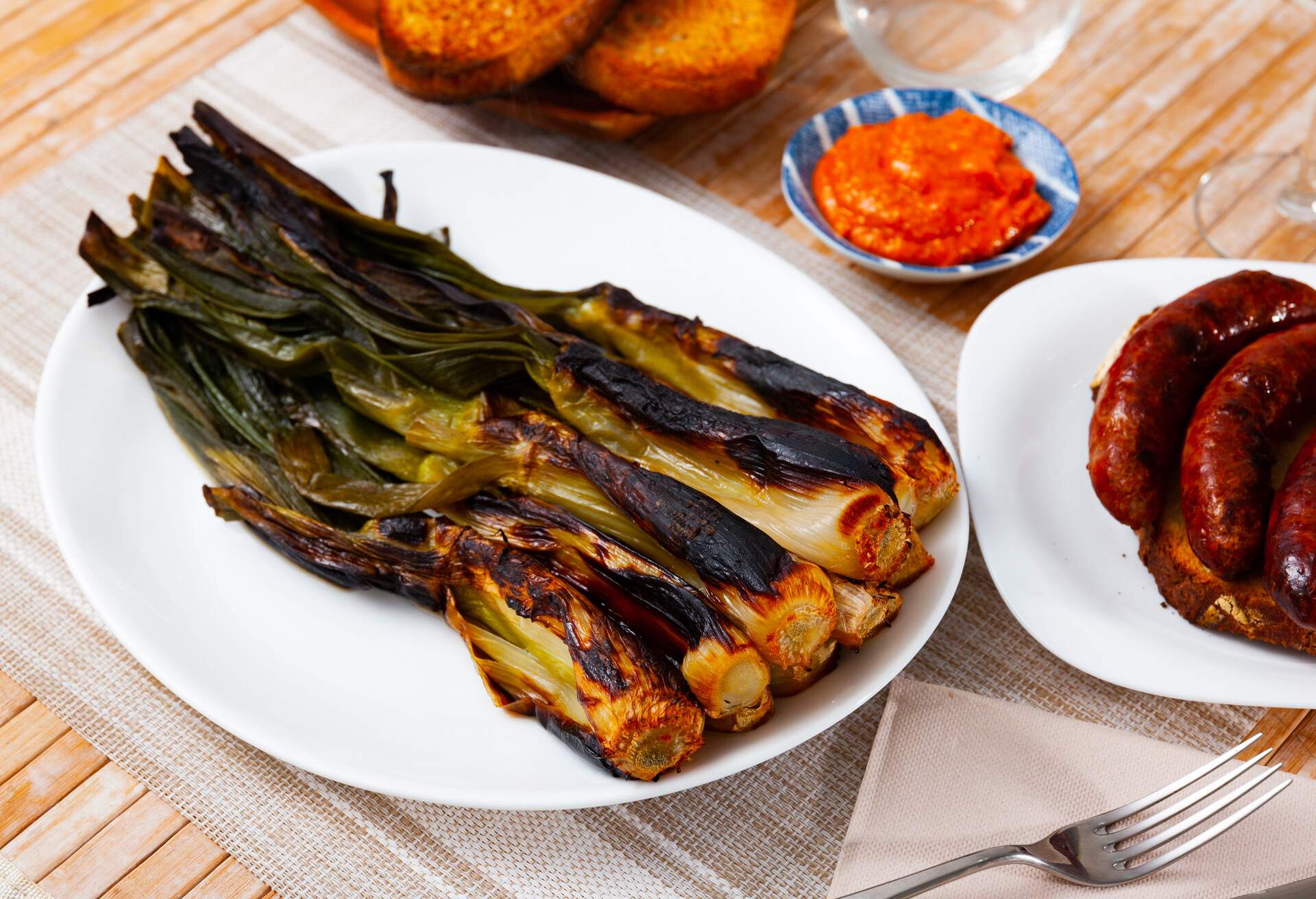 Succulent roasted calcots are enticingly served on a table alongside a flavorful romesco sauce and savoury botifarra.