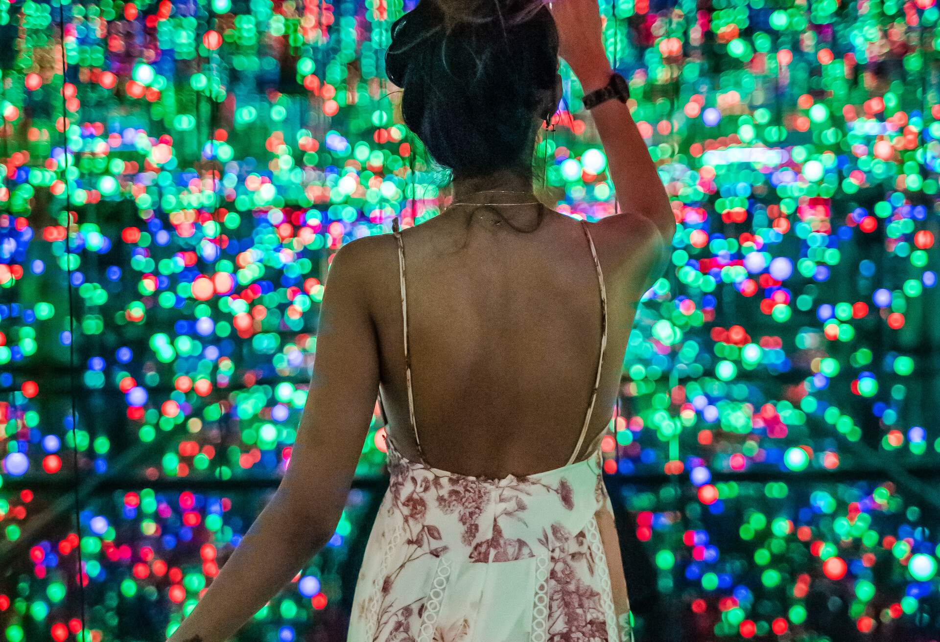 A woman in a dress pointing at small dots of red, green, and blue lights.