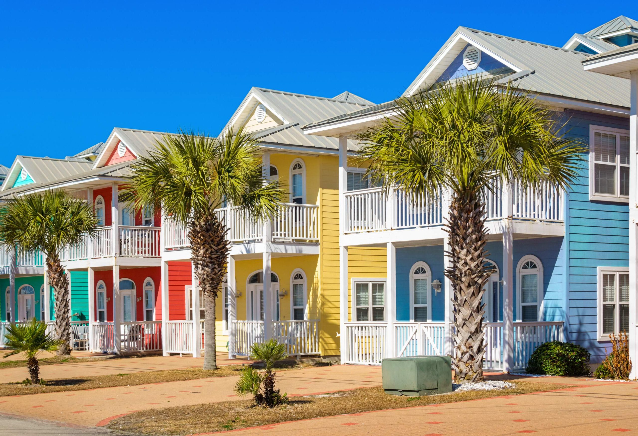 A row of colourful adjacent wooden homes with palm trees.