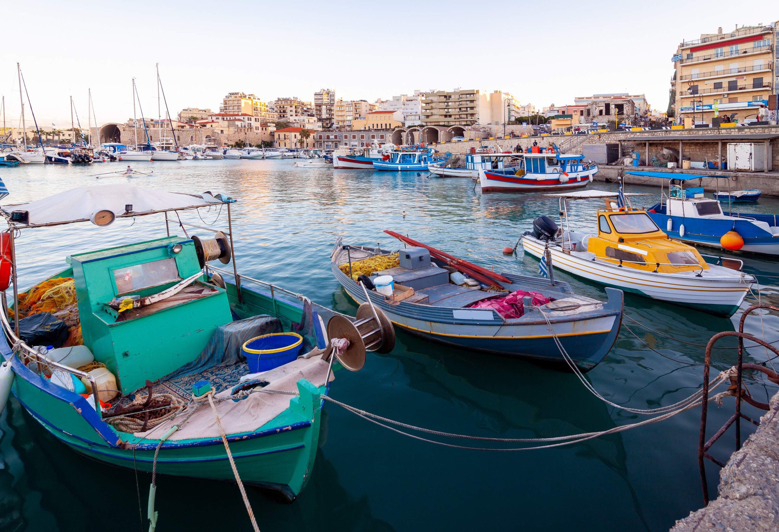 A peaceful marina with many boats moored in front of a charming seaside town with beautiful views of the coast. 