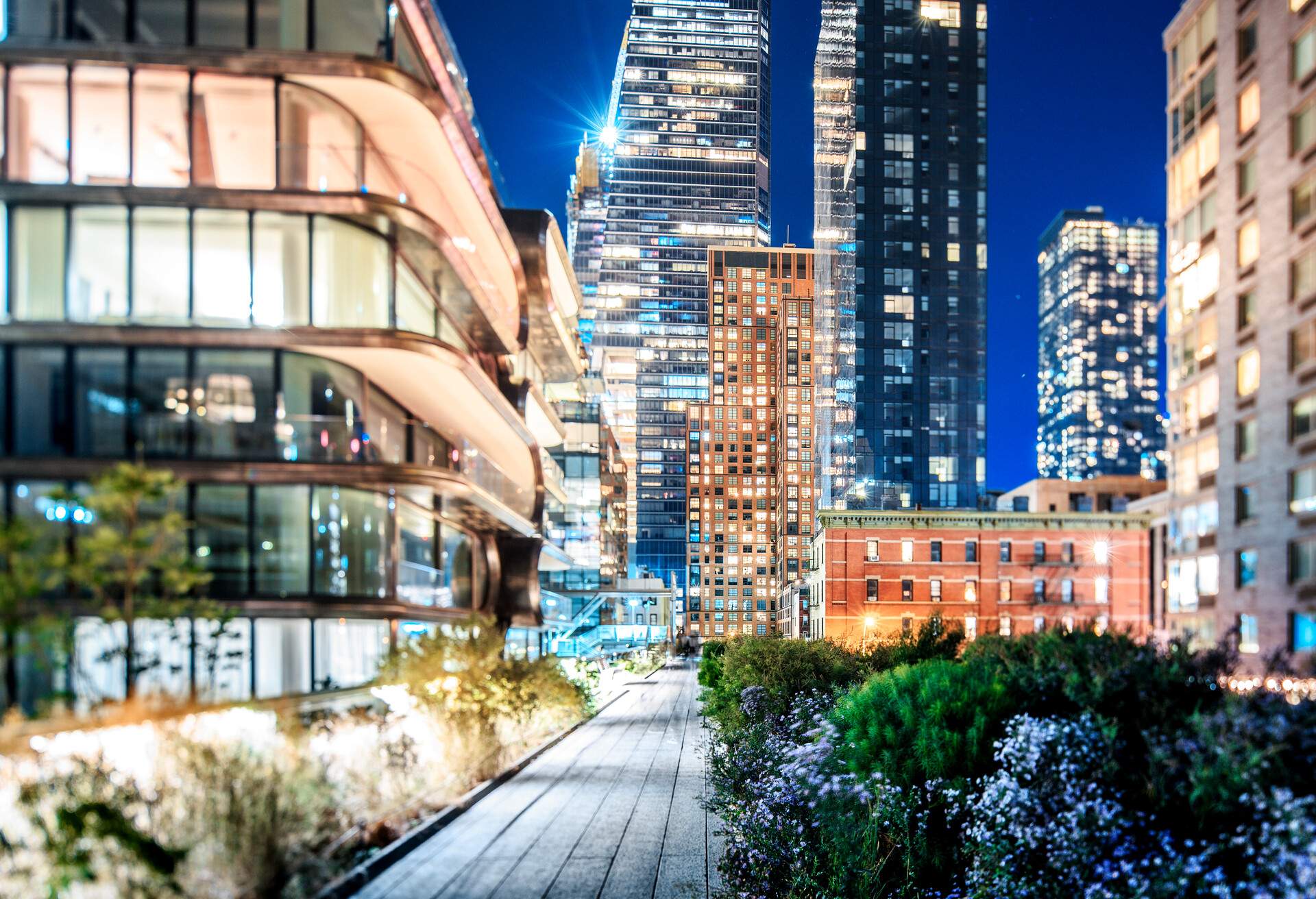 The tall skyscrapers along the High Line promenade illuminated against the night sky.