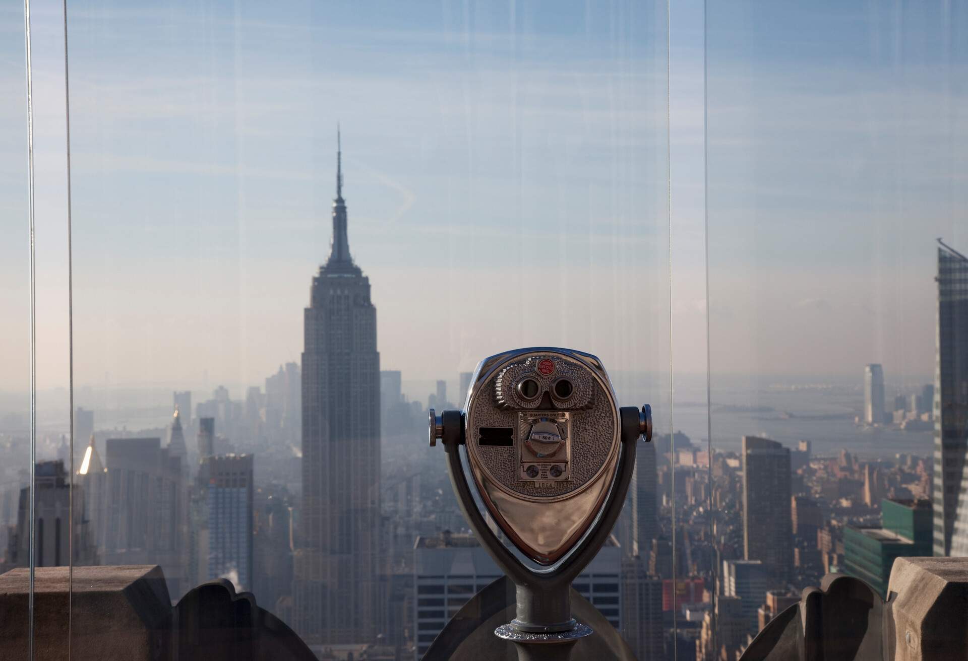A coin operated binoculars on a rooftop pointing at a vast cityscape.