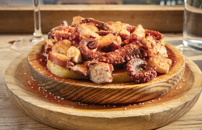 A photo of pulpo a la gallega, traditional Spanish octopus dish, served in the typical wooden bowl