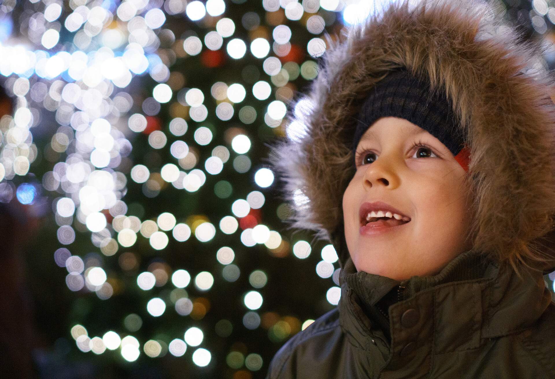 A little boy's mesmerised facial expression and blurry Christmas lights in the background.