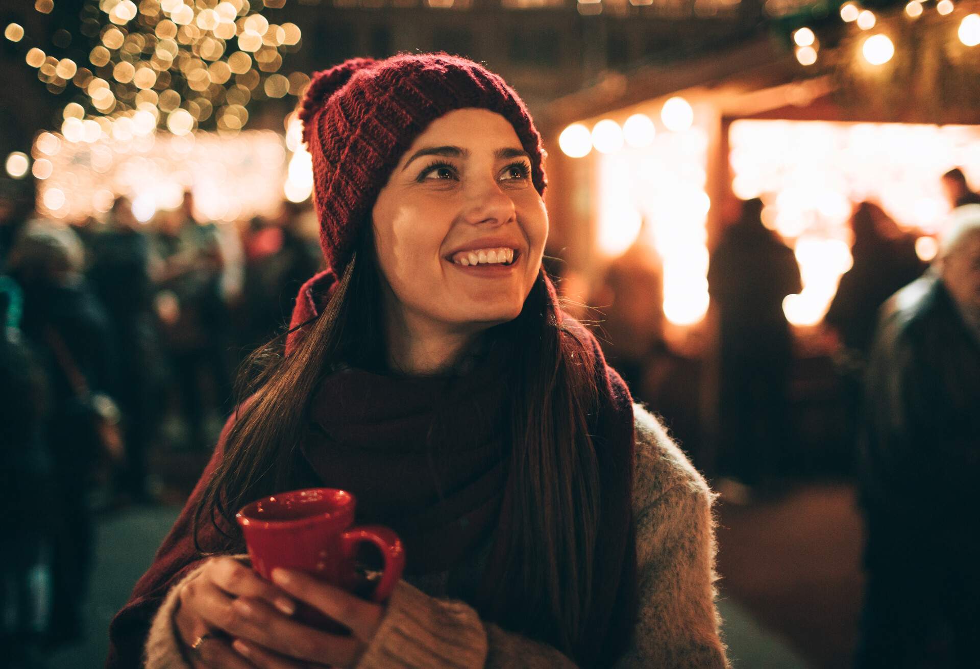 A woman in winter clothes holding a red mug and smiling while looking up