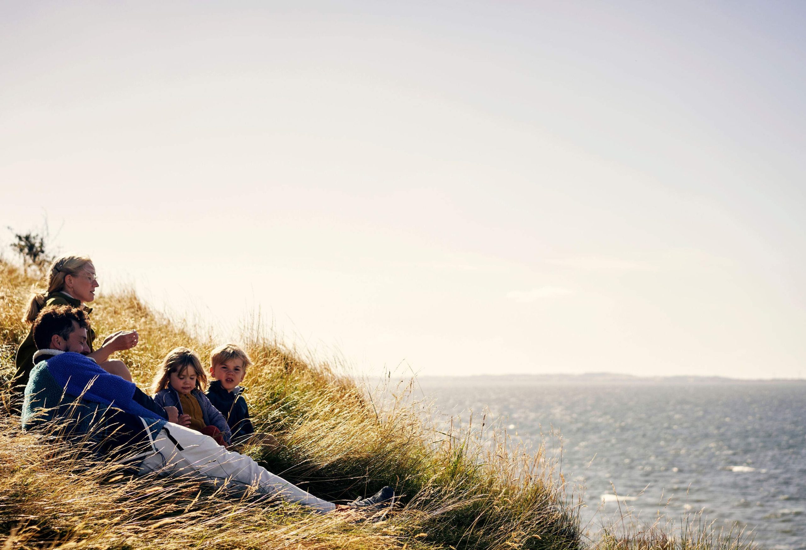 A family sitting in a field of tall grass on a hill overlooking the sea.