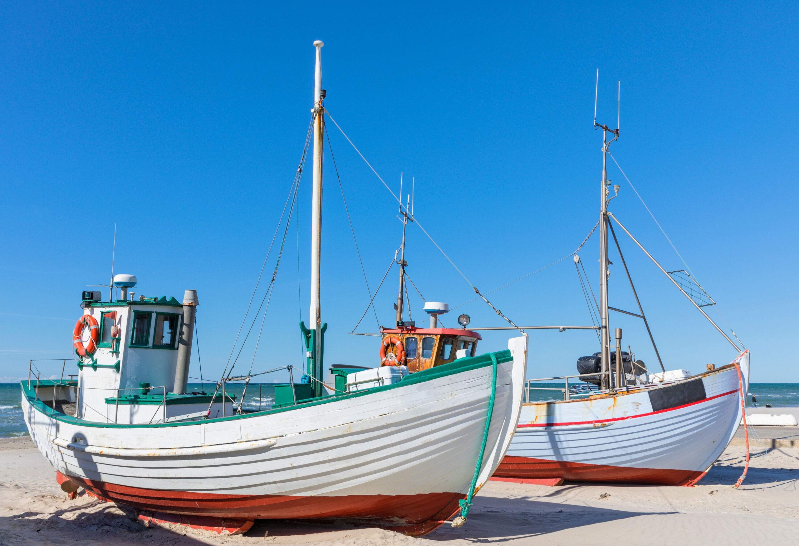 Two fishing boats on fine white sands against the clear blue sky.