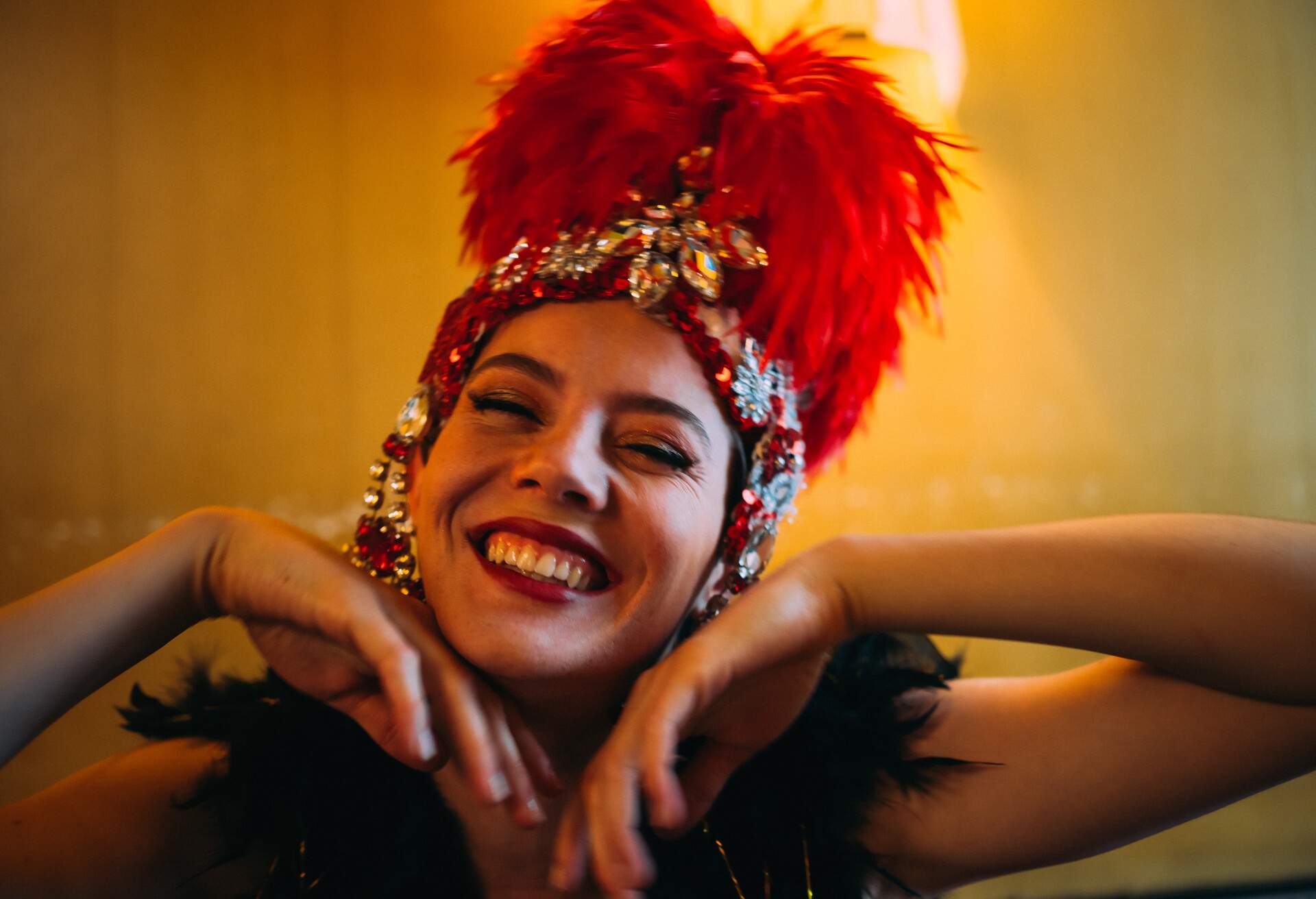 A person with a red feathered headpiece and black feathered top smiles happily.