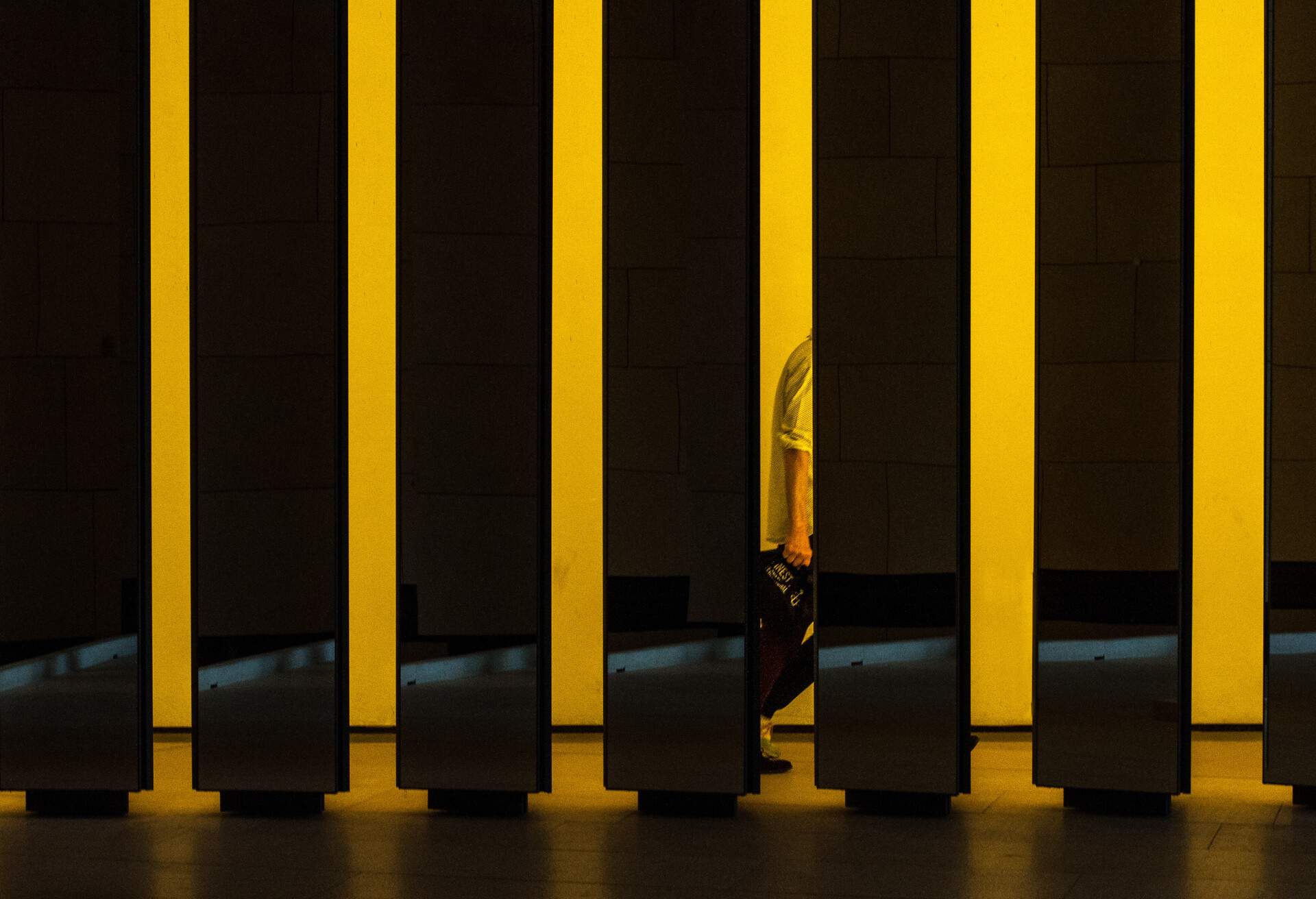 A series of yellow columns, one of which has a reflection of a person's half-body.