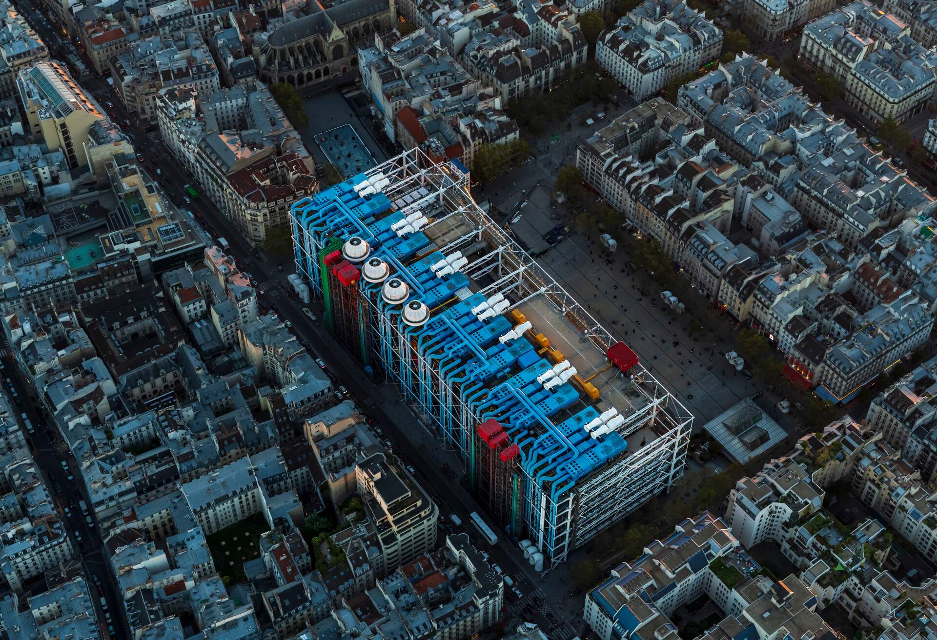 A city's urban landscape surrounds Pompidou Centre, a rectangular cultural centre with glass panelling and multi-coloured steel pipe design.