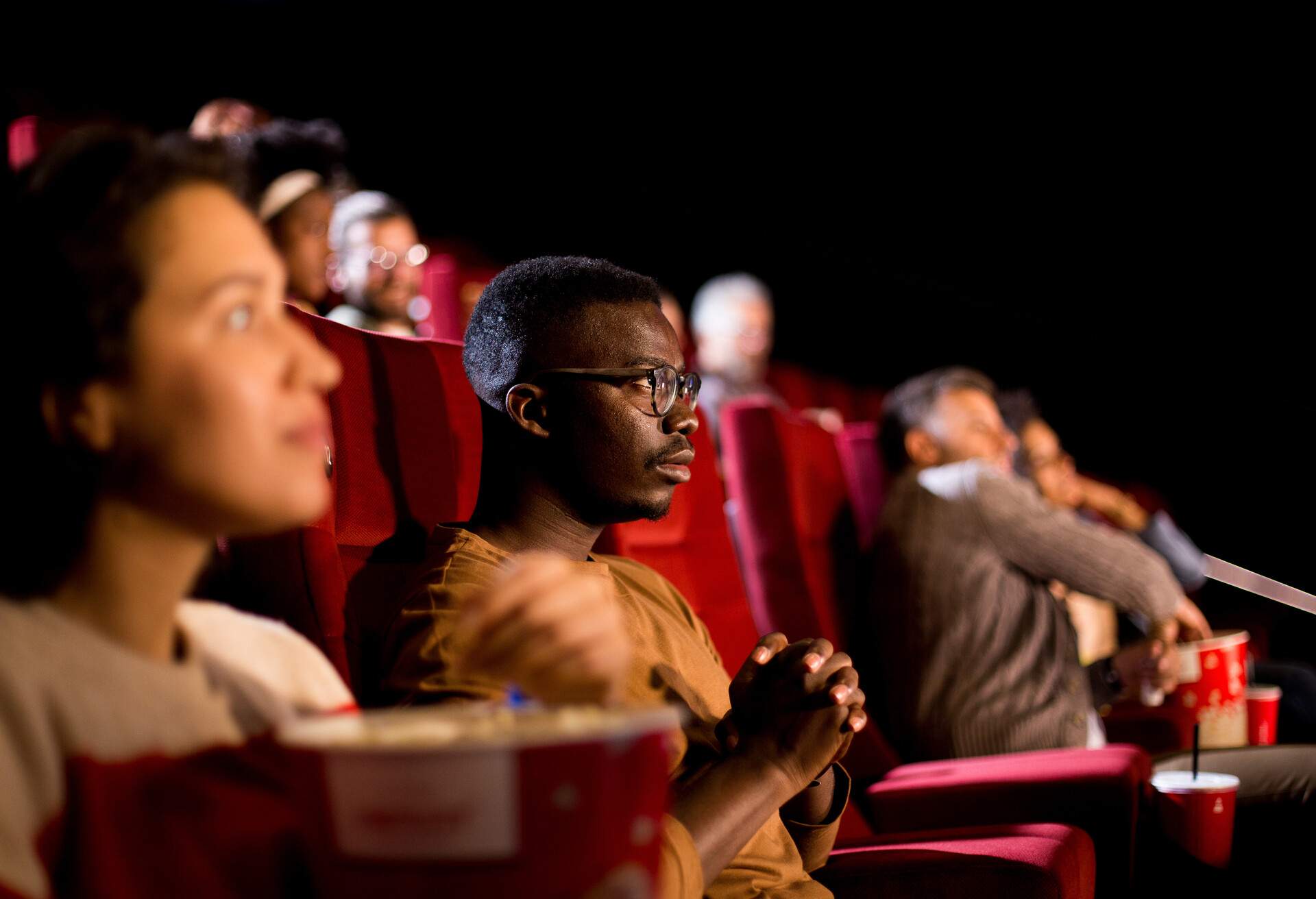 An African-American man fully immerses himself in the cinematic experience, eyes fixed on the screen, his delighted expression reflecting the enjoyment and escape that movies can provide.