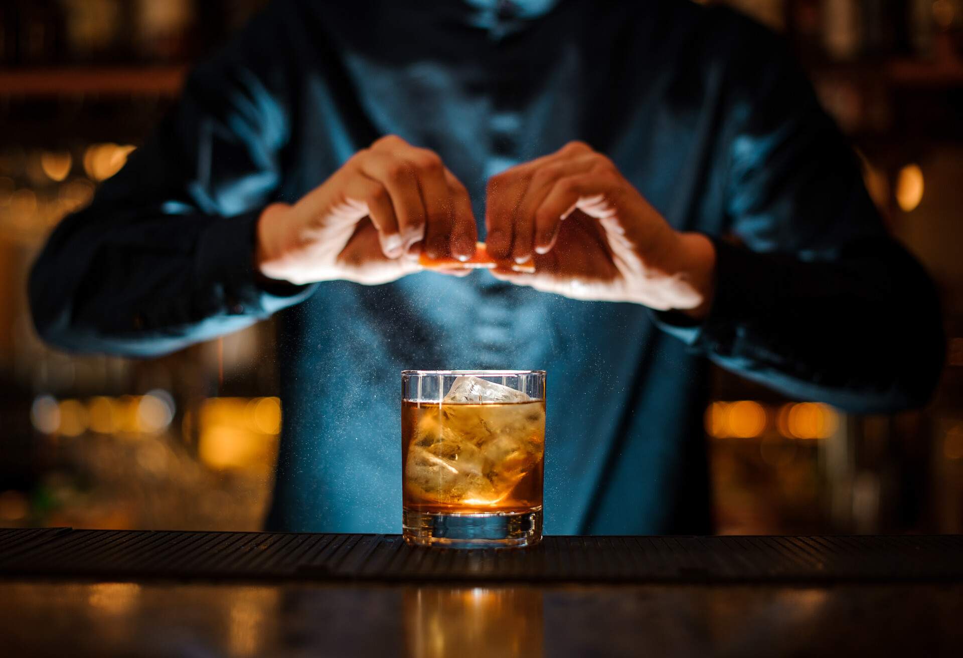 A bartender squeezes an orange over a glass of cocktail drink.