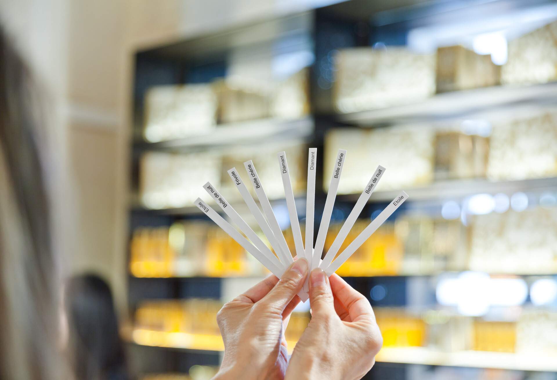 Hands showing a set of different perfume test strips inside a boutique shop.