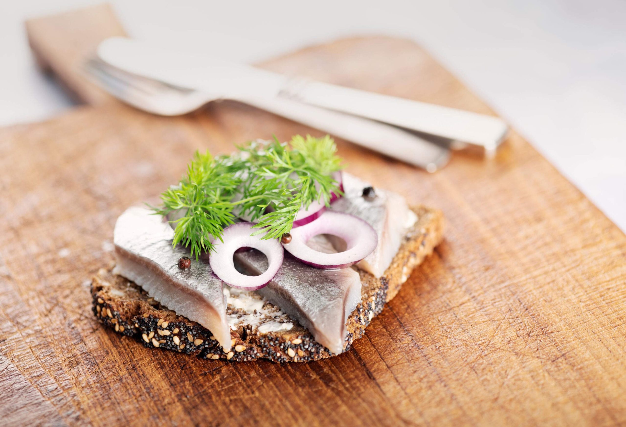 A dense, dark brown bread topped with pieces of fish, onion, and dill.
