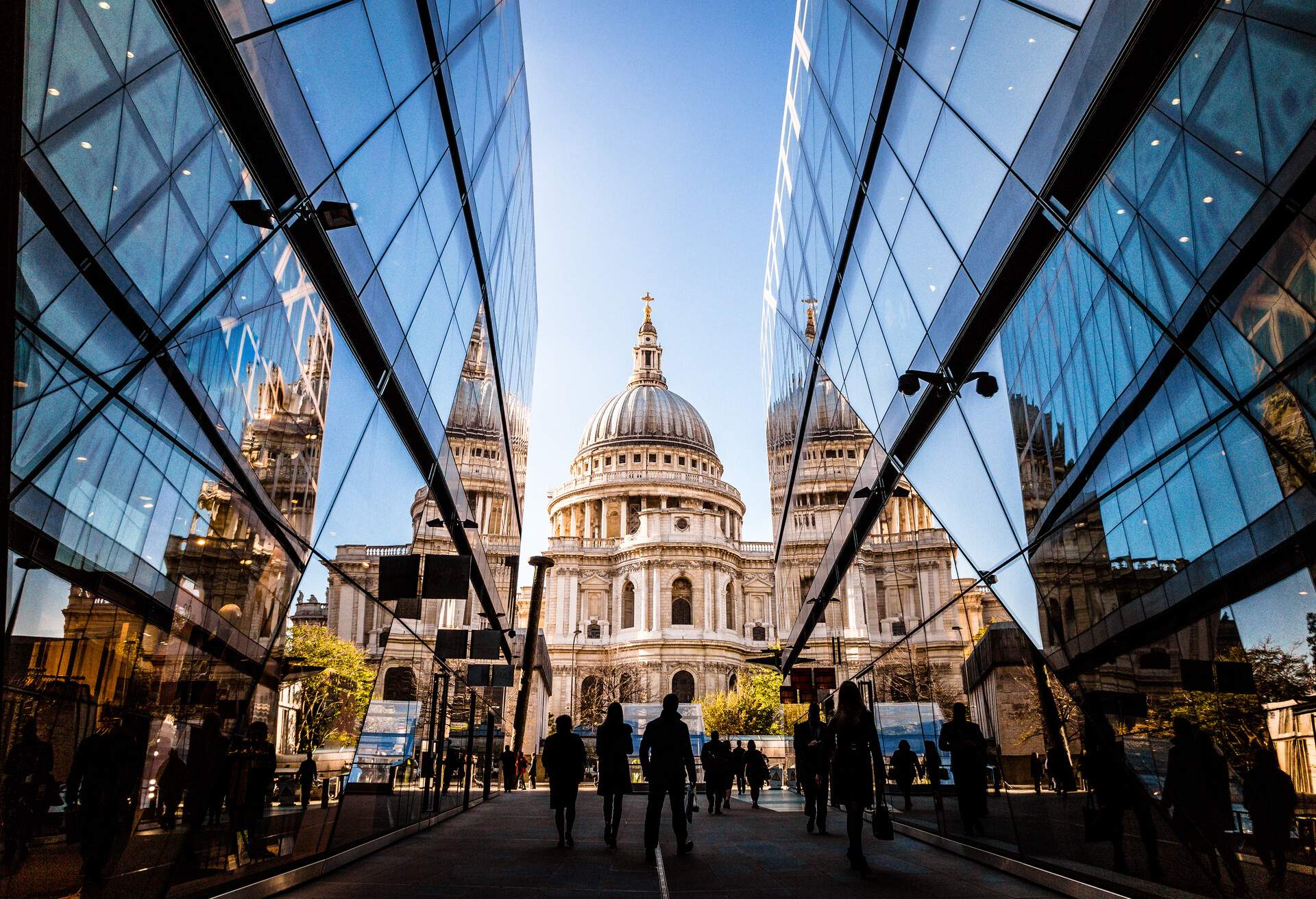 Color image depicting a crowd of people, thrown into silhouette and therefore unrecognisable, walking alongside modern futuristic architecture of glass and steel. In the distance we can see the ancient and iconic dome of St Paul's cathedral. Room for copy space.