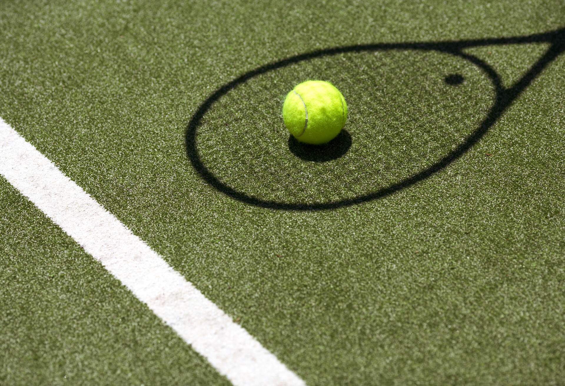 Tennis ball with racket shadow on grass court.