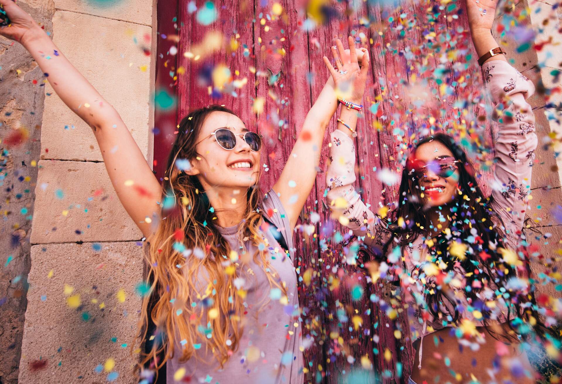 Cheerful multi-ethnic female teenage best friends partying by throwing confetti in city streets