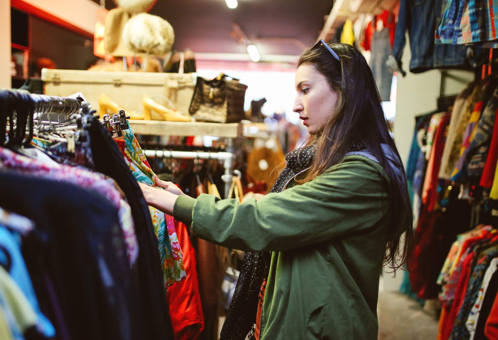 Long-haired brunette woman browsing through clothes on a rack at a thrift store.
