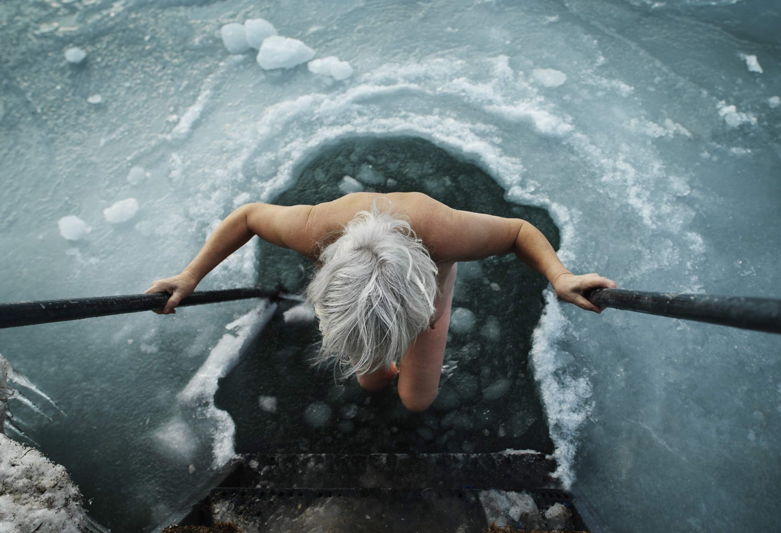 Elderly woman entering the frozen sea through a hole in the ice.