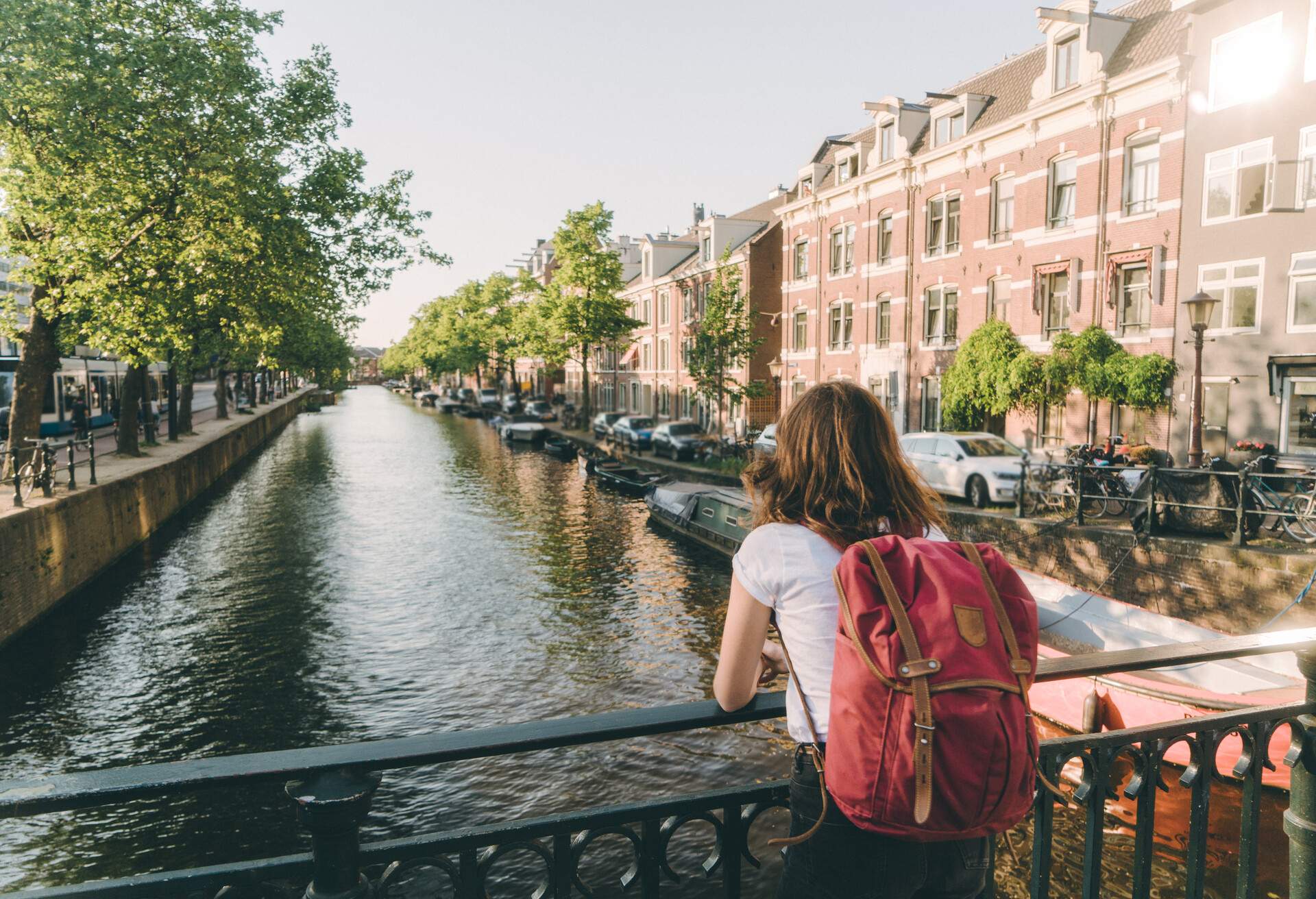 A woman with a backpack leaning on a bridge railing as she looks over a canal.