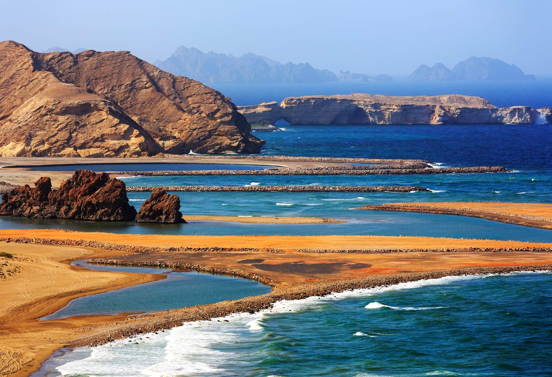 The blue sea flooding over the golden sand beach protected by rugged rock formations.