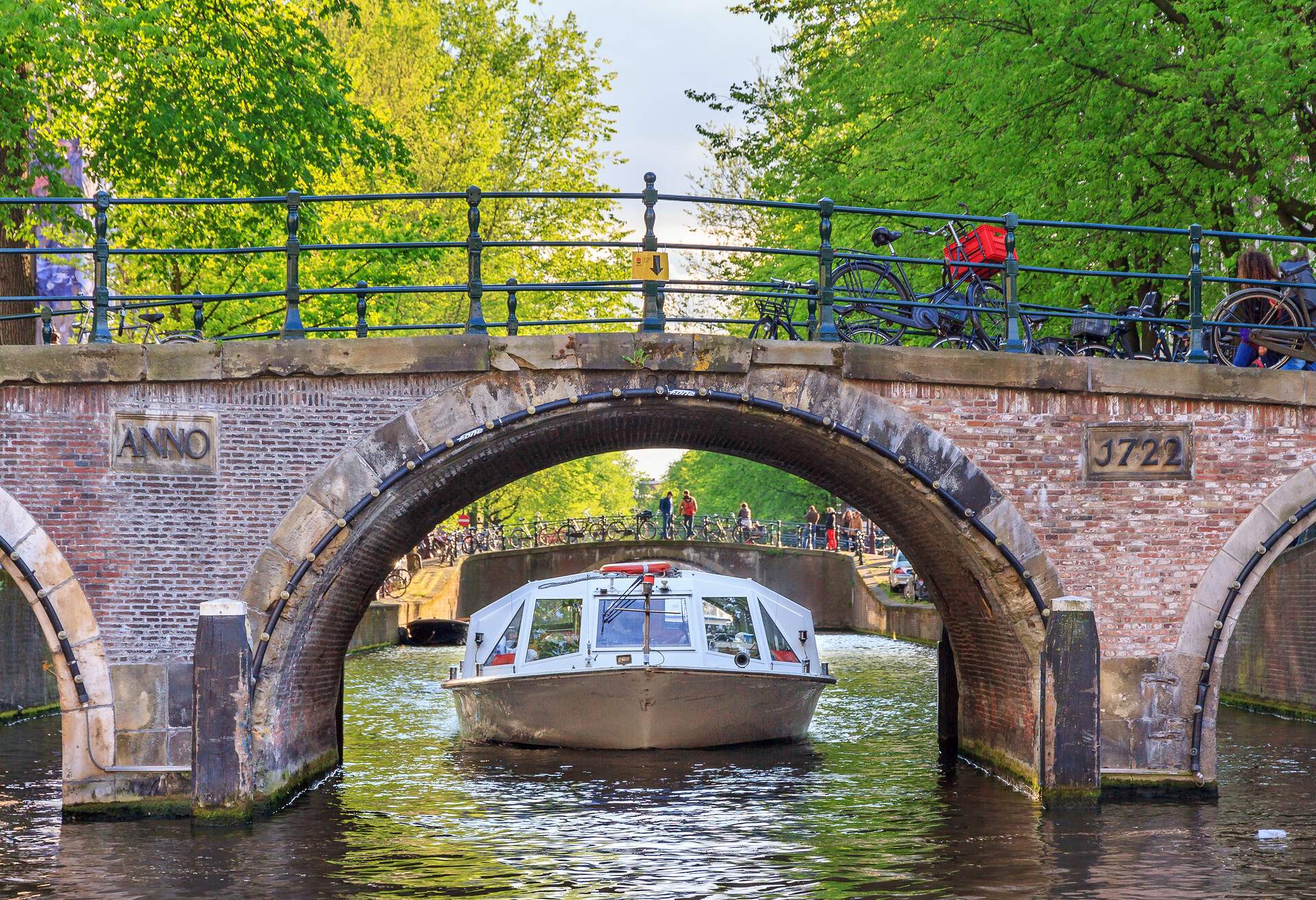 A canal boat with passengers about to pass through an arch bridge.