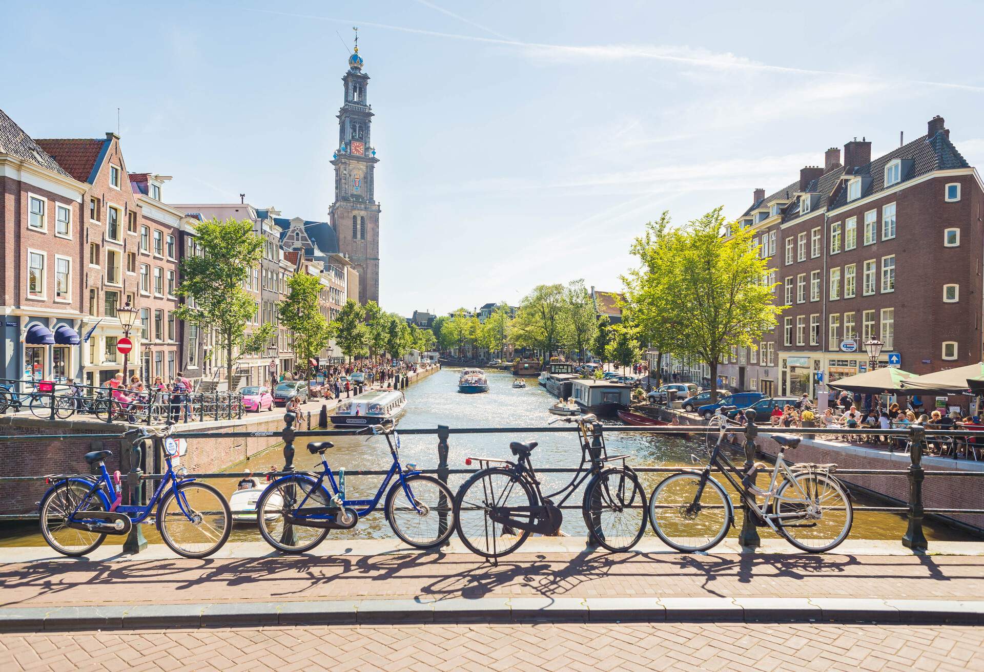 A city canal with bikes parked on the side of a bridge and people walking along towpaths.