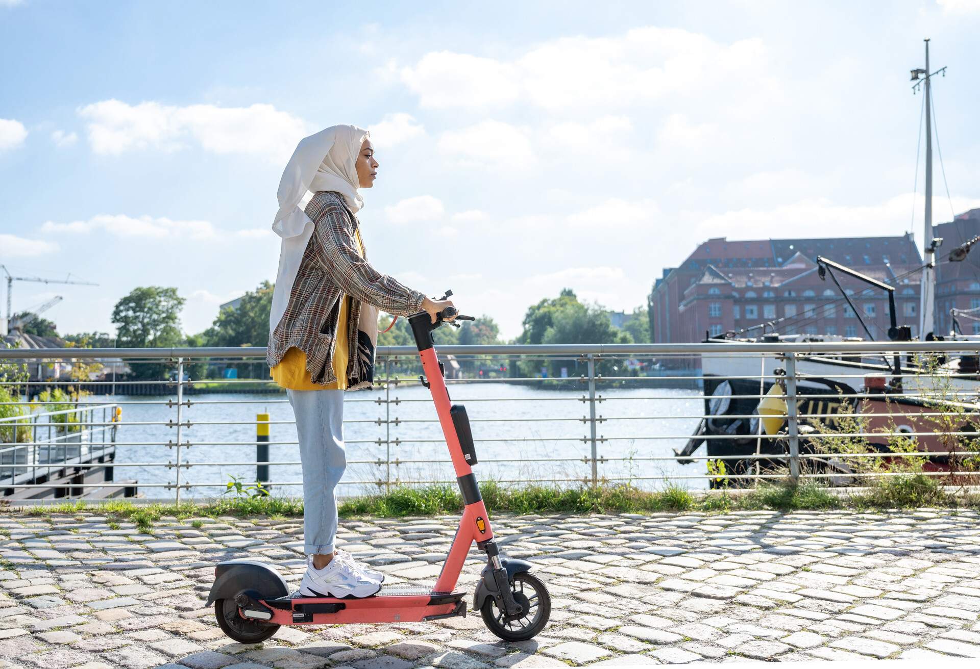 A woman in a hijab rides an e-scooter along the river.